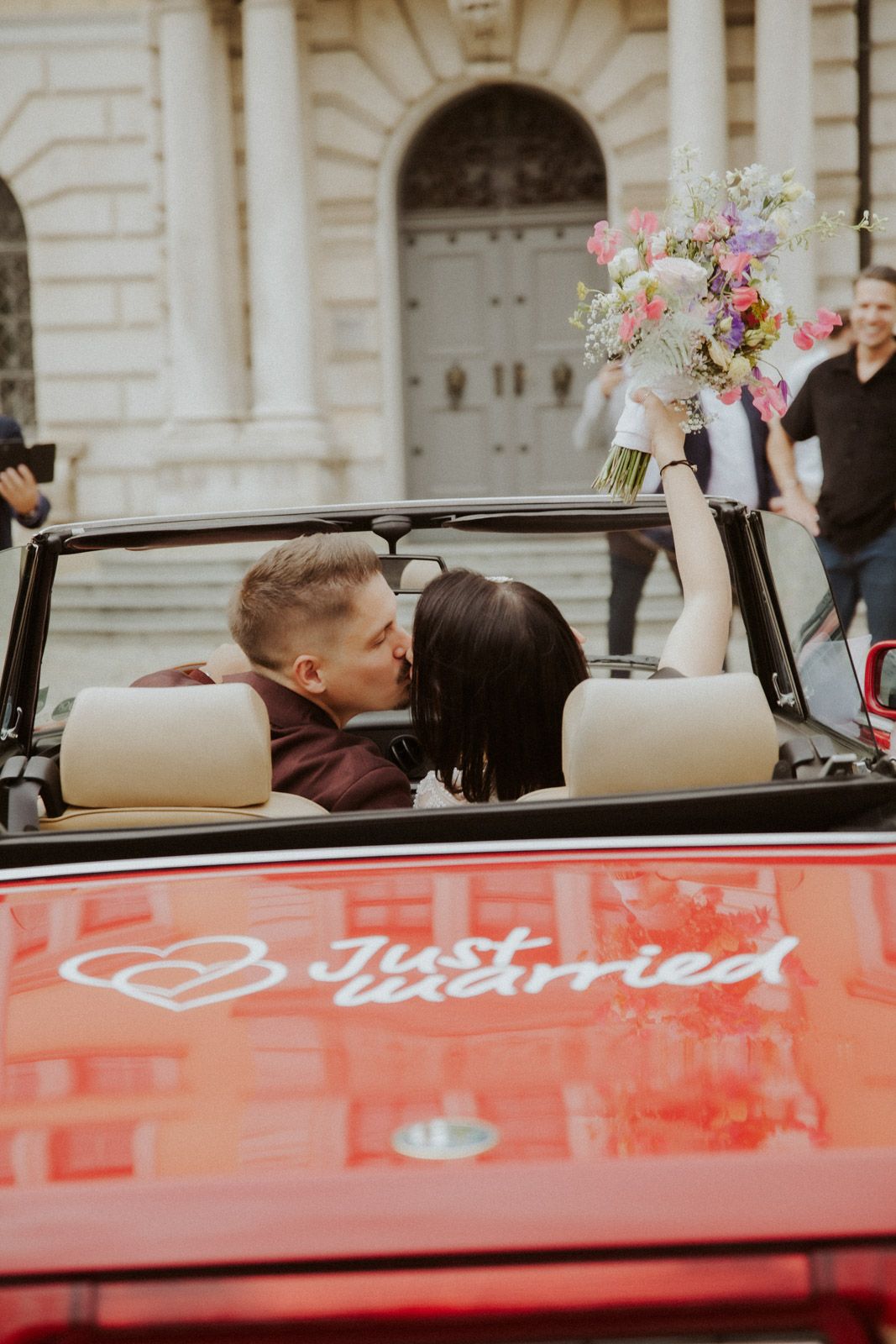 Brautpaar fährt in einem roten Just-Married Cabrio davon