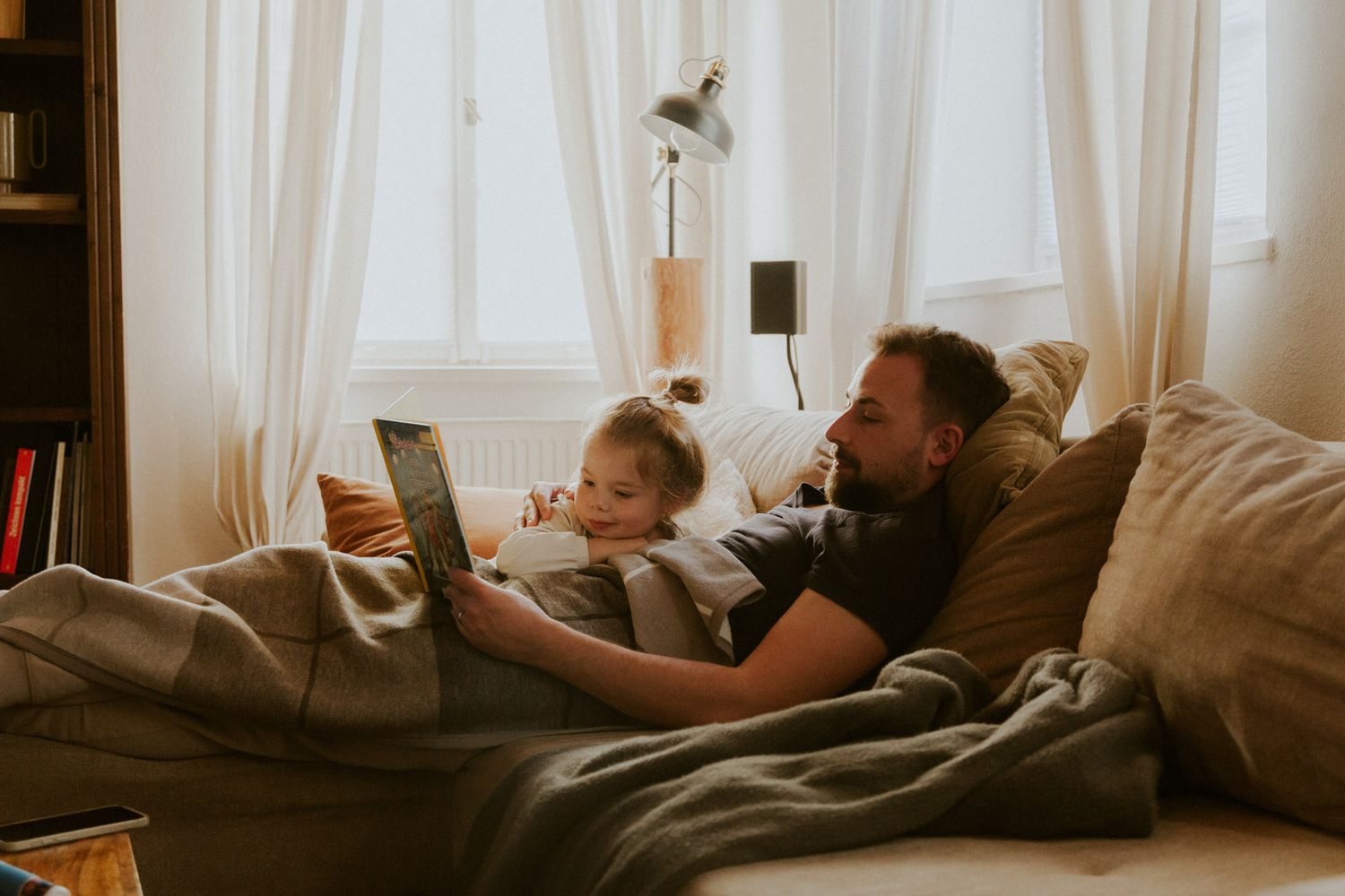 Vater liest mit seiner Tochter auf der Couch am Morgen