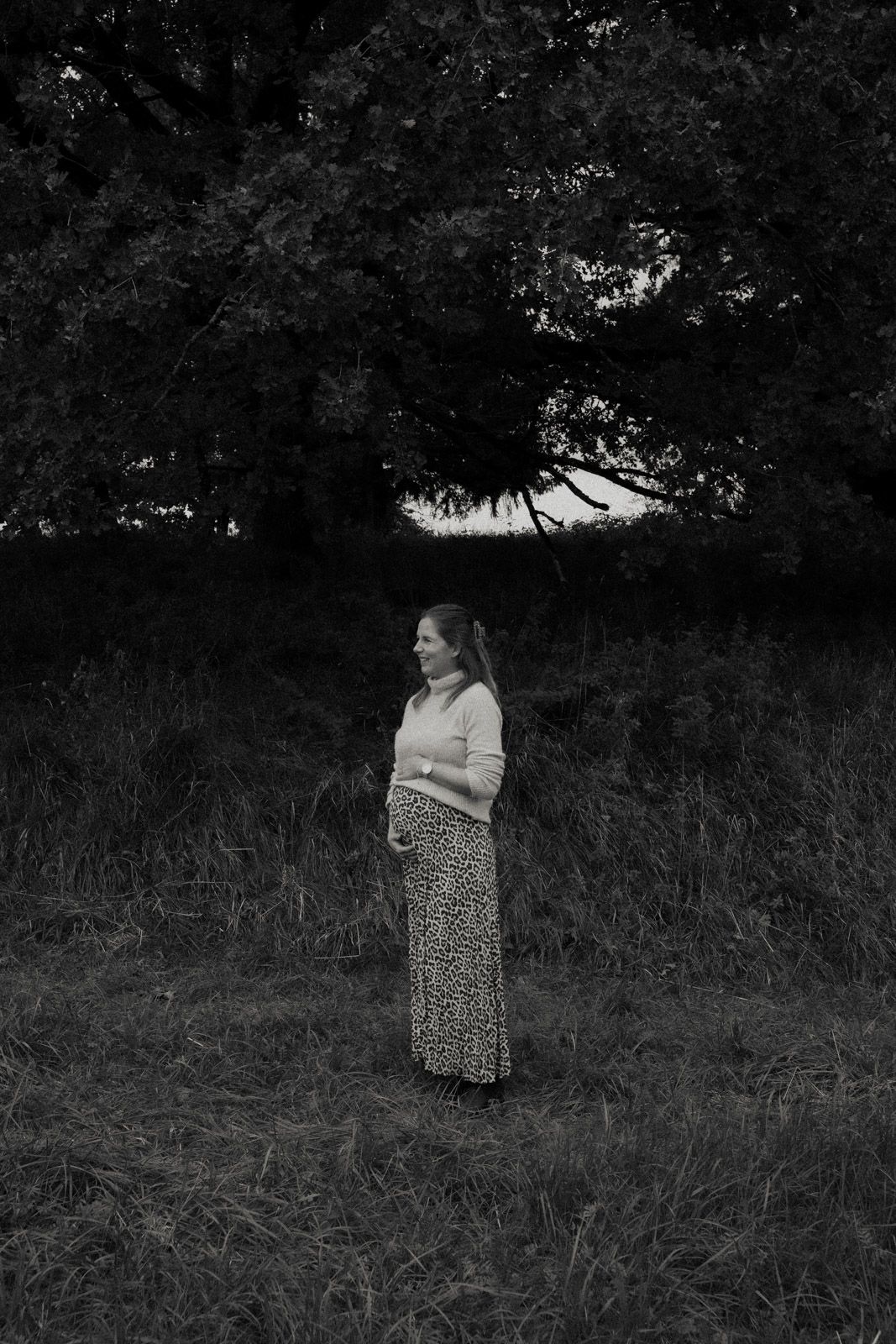 Schwangere Frau steht allein unter einem Baum – Schwarz-Weiß Babybauchfotografie