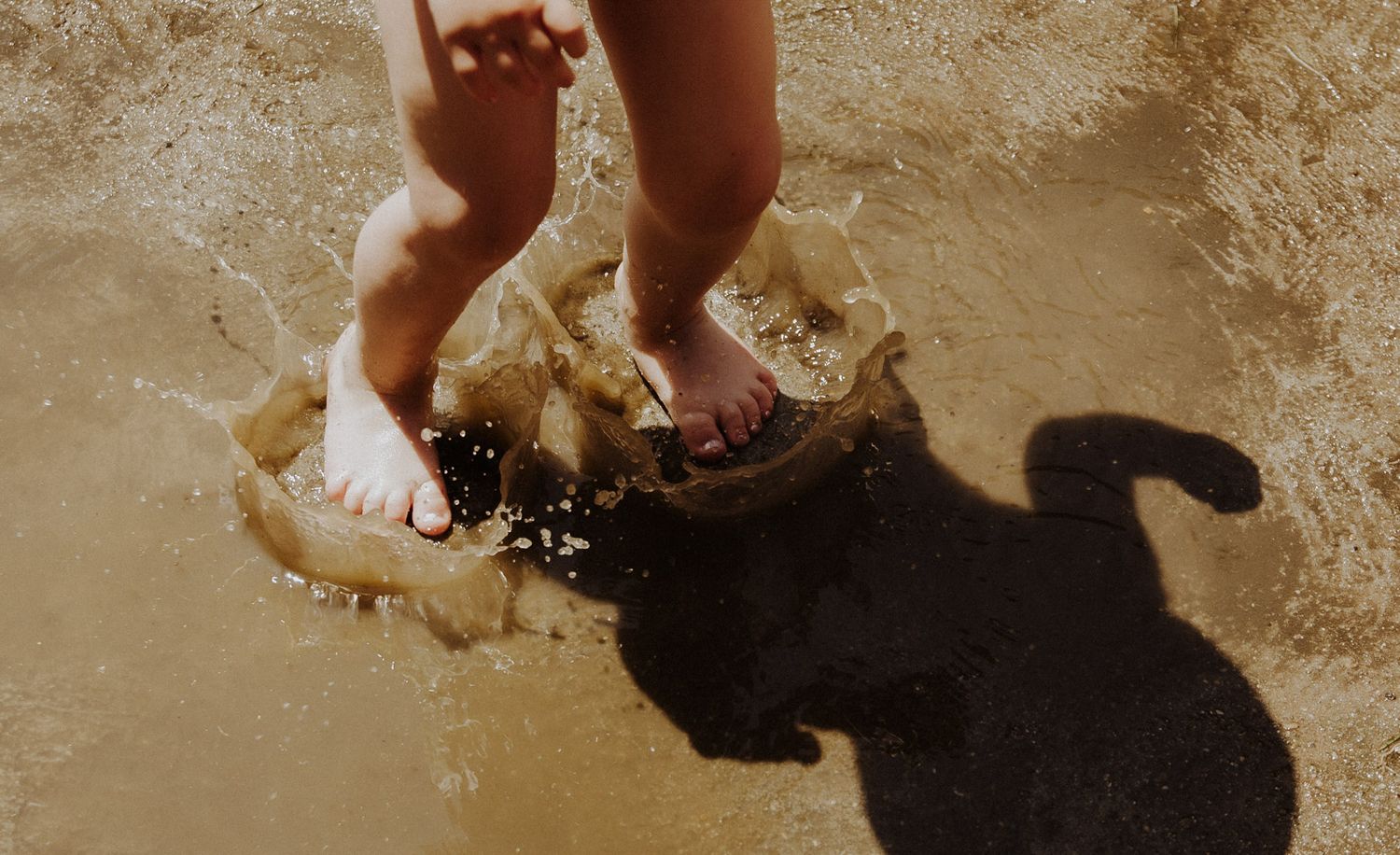 Kinderfüße plantschen ausgelassen in einer Wasserpfütze – authentische Kinderfotografie Ingolstadt