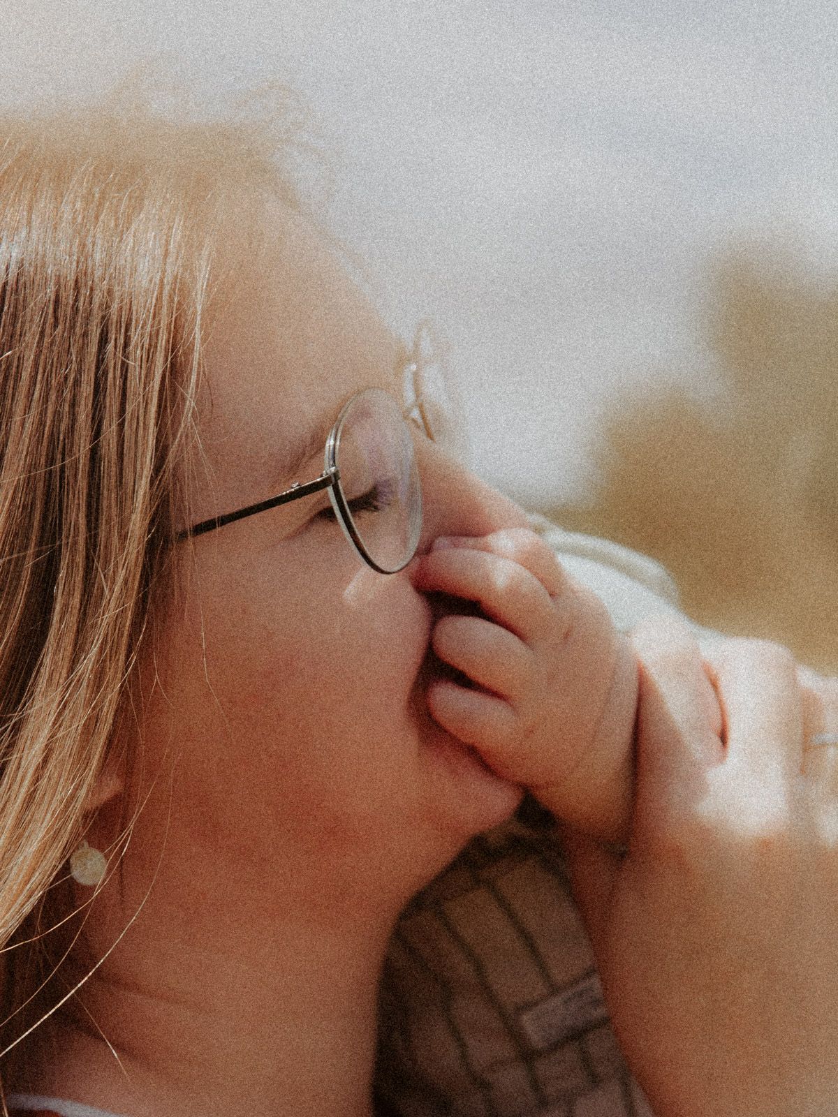 Nahaufnahme Frau mit Brille küsst Hand vom ihrem Baby