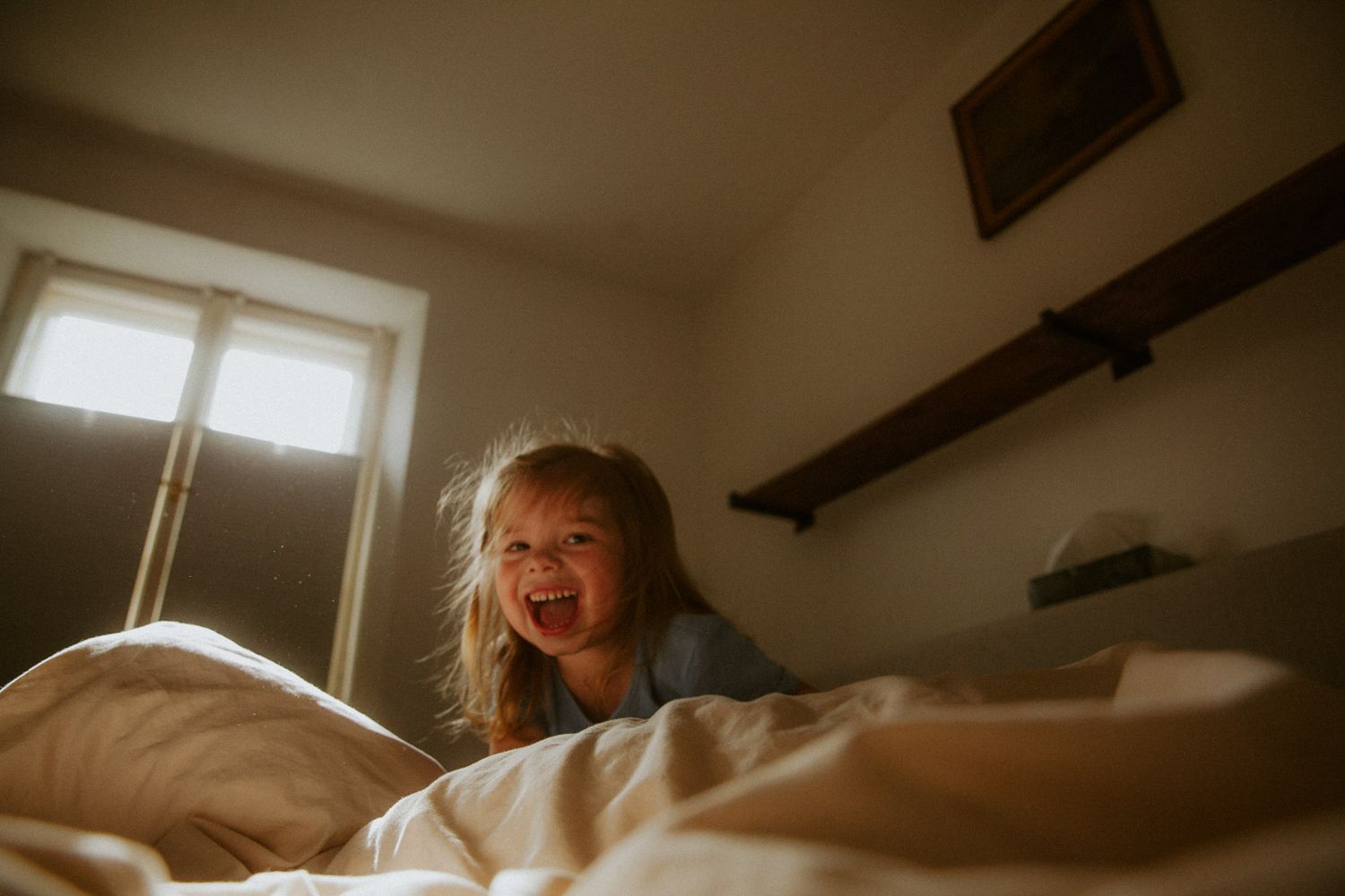 Lachendes kleines Mädchen auf dem Bett – authentische Familienfotografie Ingolstadt