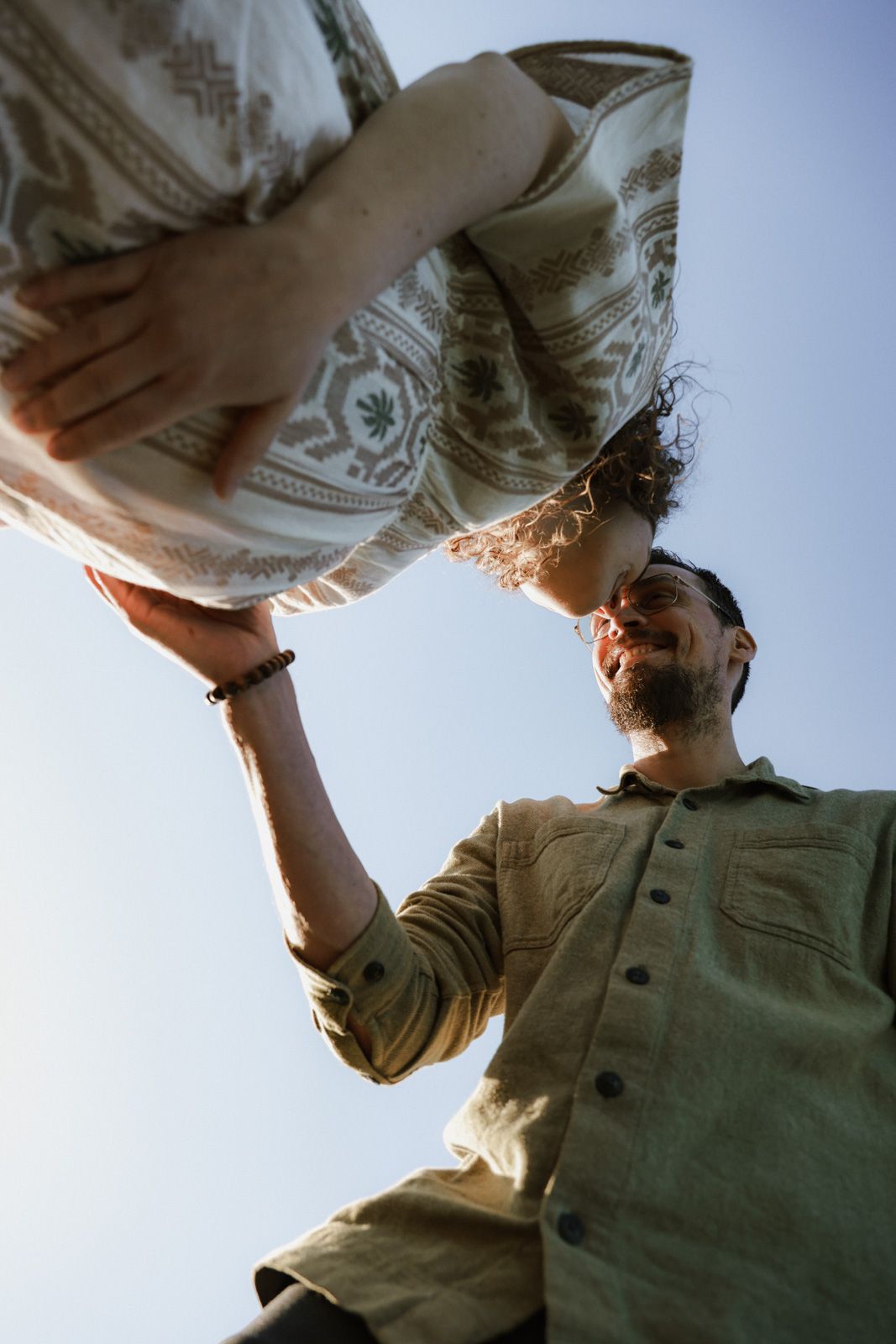 Vater hebt Partnerin hoch – Froschperspektive Babybauchshooting