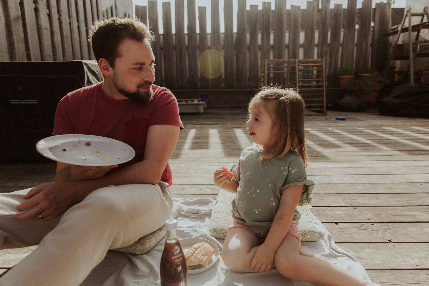 Vater und Tochter sitzen im Sonnenlicht auf der Terrasse und schauen sich an – Familienfotografie Ingolstadt