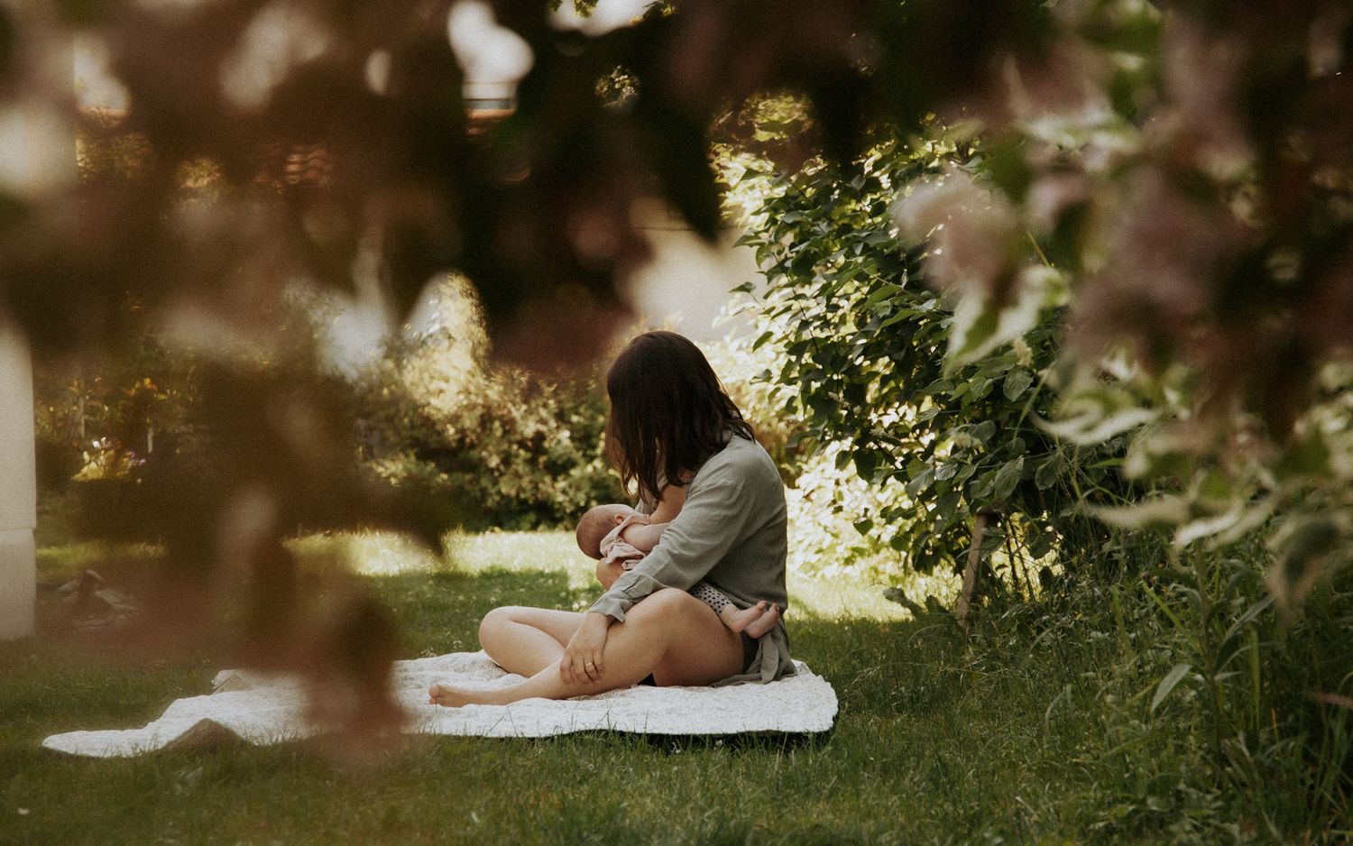 Mutter stillt ihr Baby entspannt im Garten unter Bäumen – authentische Familienfotografie