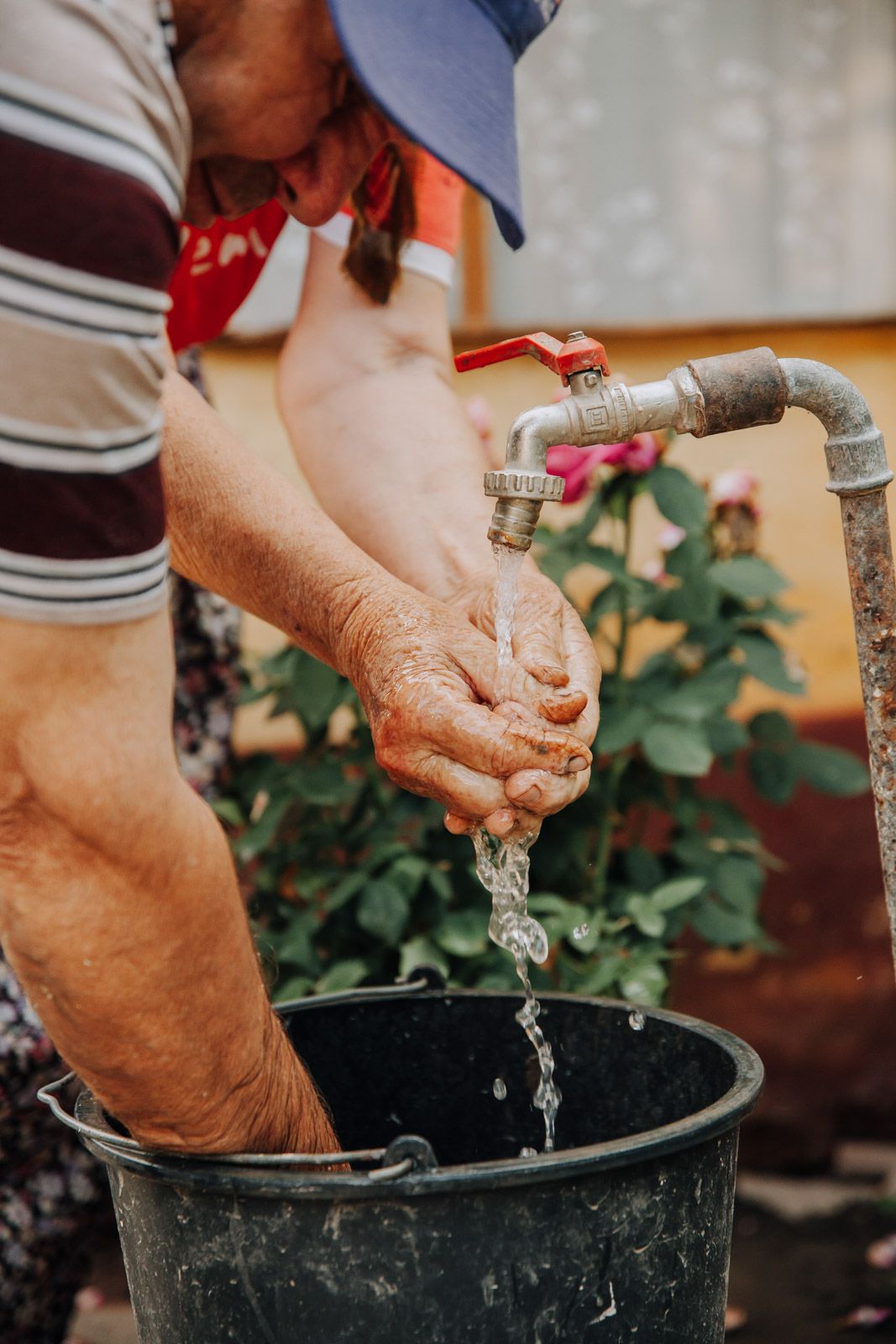 Mann wäscht Hände an einem Wasserhahn im Garten