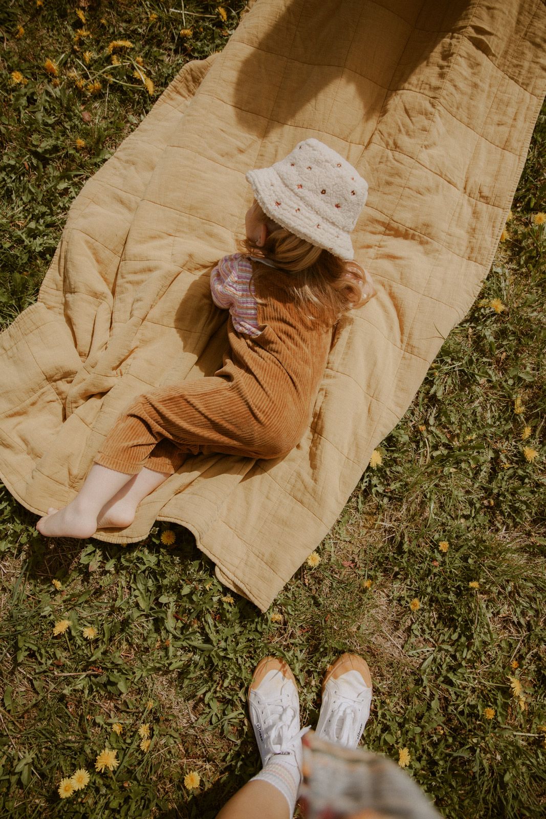 Kleines Mädchen mit Sonnenhut liegt entspannt auf einer gelben Decke im Gras – Kinderfotografie