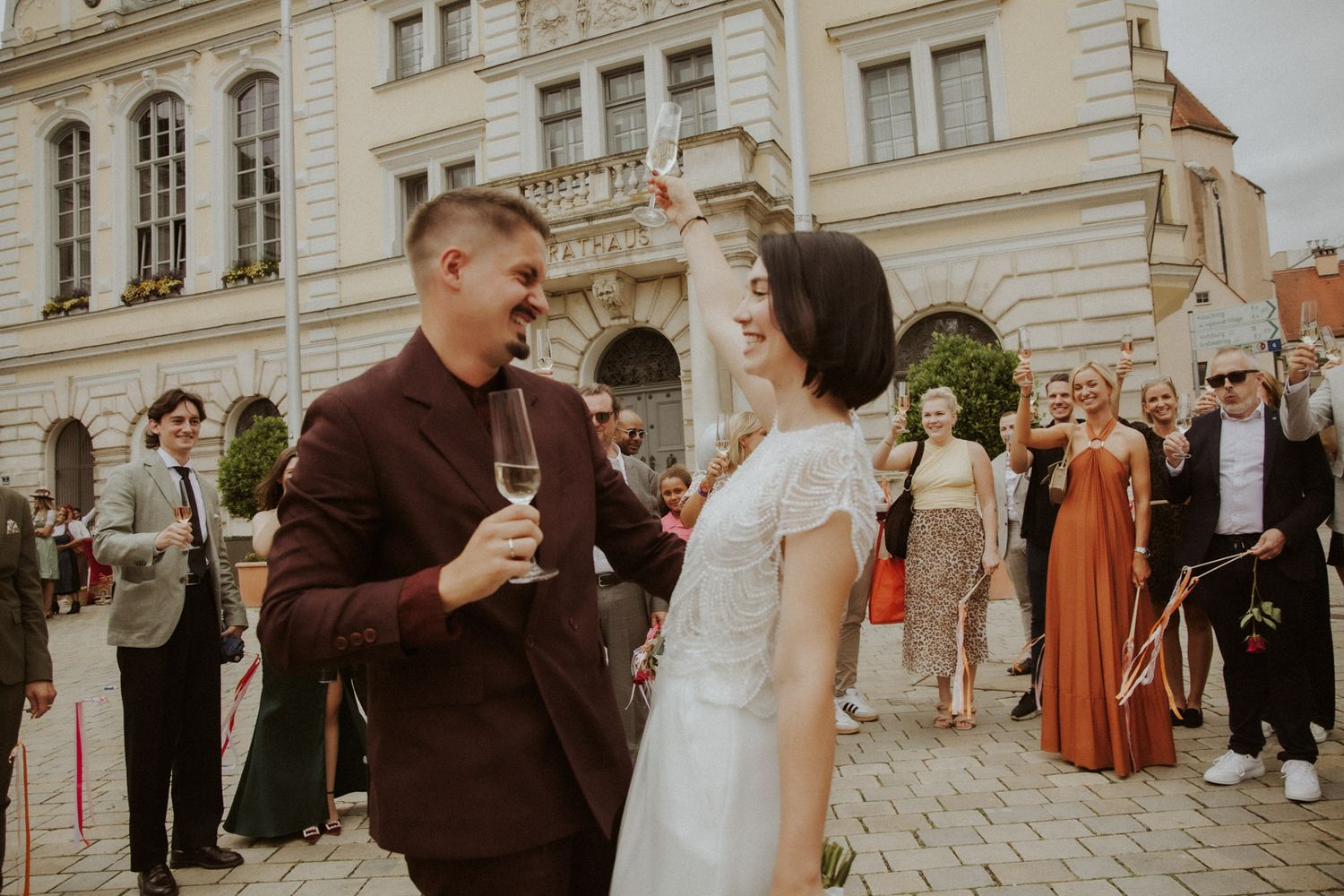 Bräutigam stößt lachend mit Champagner an vor historischer Kulisse