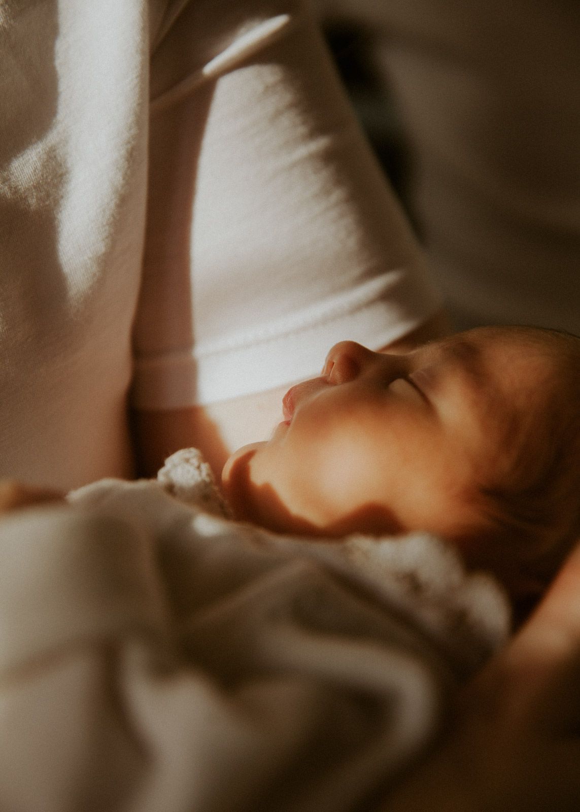 Neugeborenes schläft friedlich auf dem Arm der Mutter im warmen Licht
