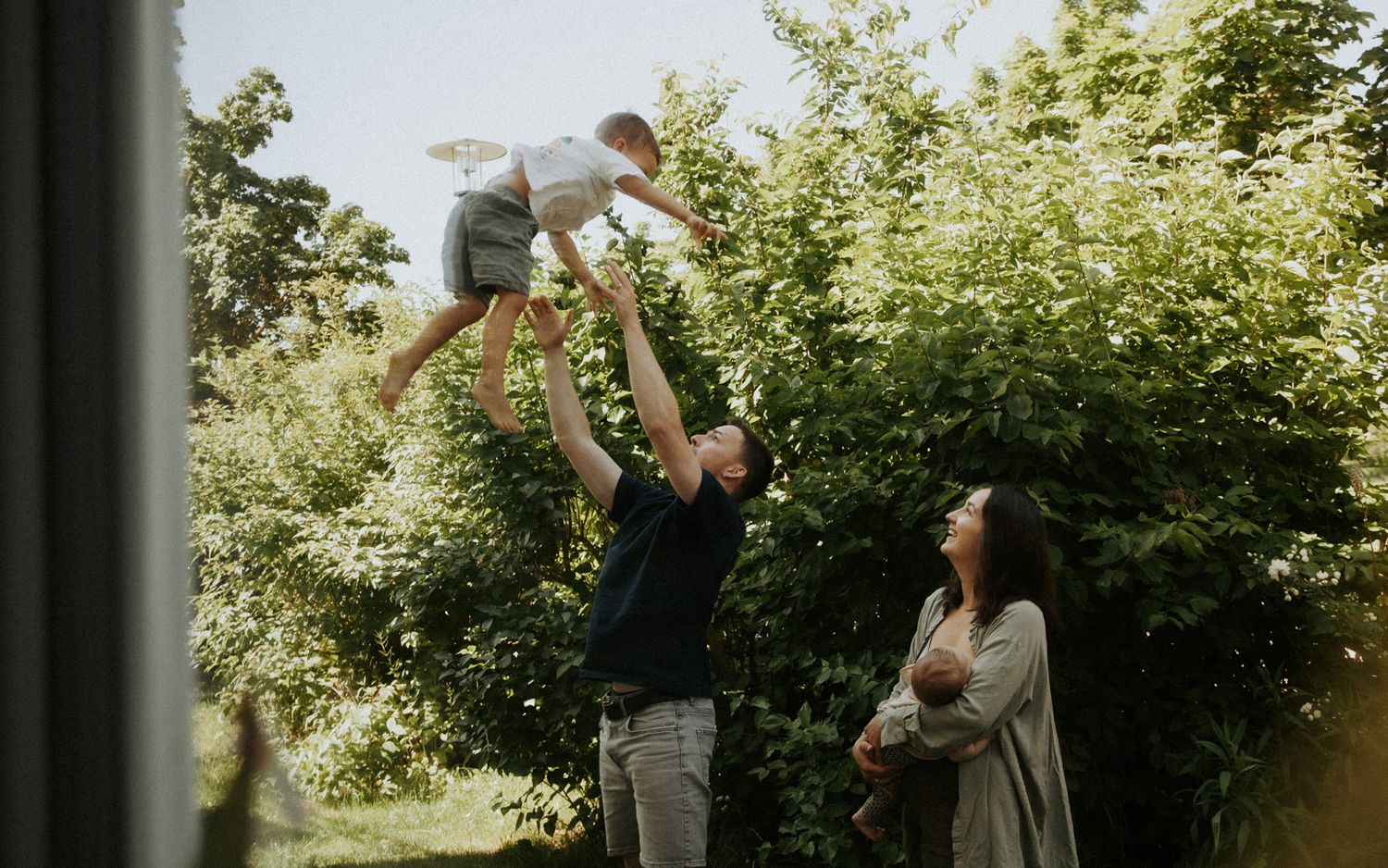 Vater hebt lachend sein Baby in die Luft im Garten