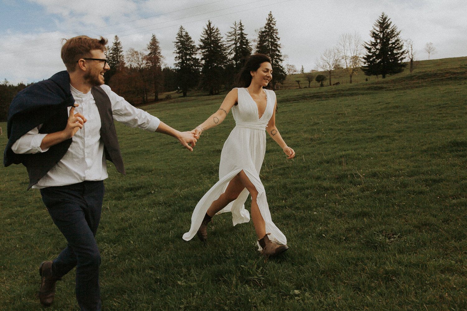 Brautpaar läuft lachend Hand in Hand über eine grüne Wiese – Hochzeitsfotografin Ingolstadt