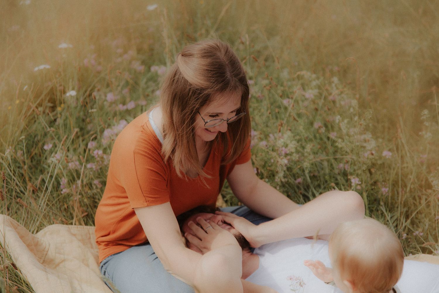 Mutter und Vater genießen die Sonne ihrem Baby in der Blumenwiese
