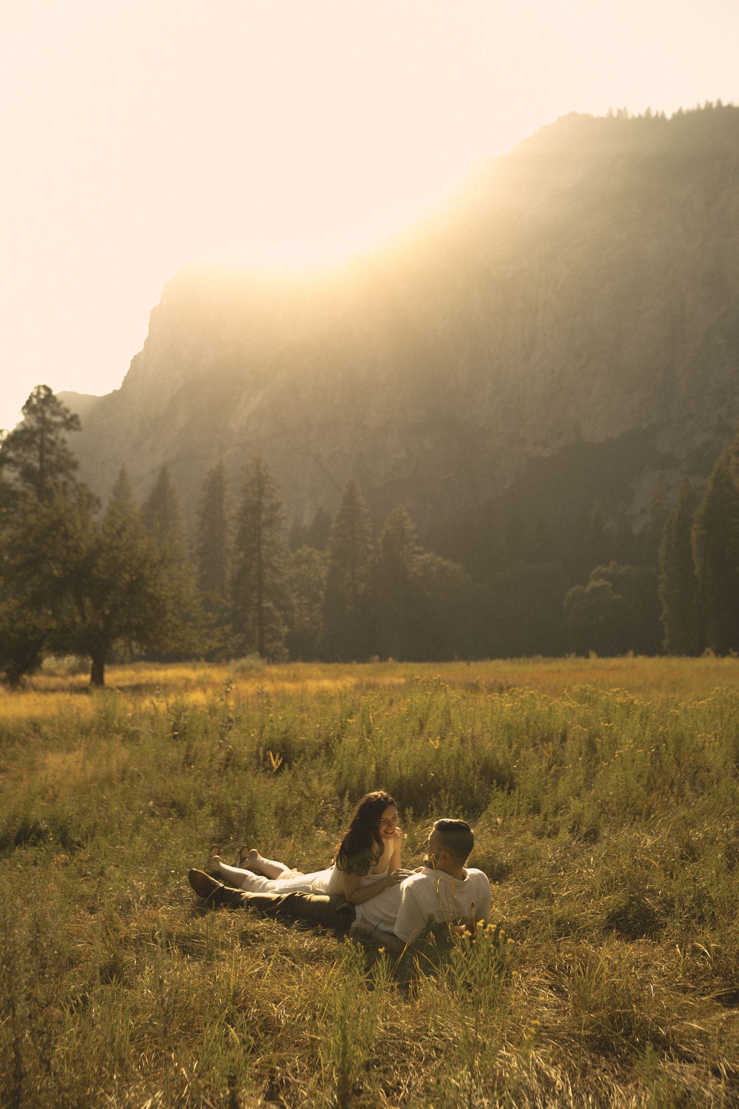 Couple sitting together in a golden sunlit meadow with mountain backdrop at sunset in Yosemite Valley.
