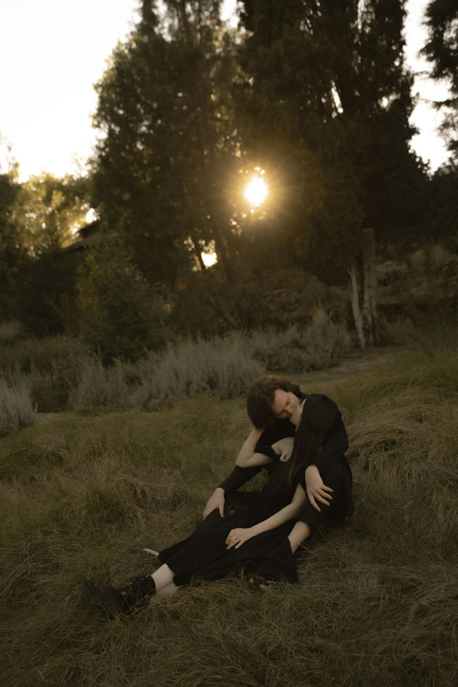 A couple sits together on a grassy hillside bathed in warm golden sunset light outdoors.