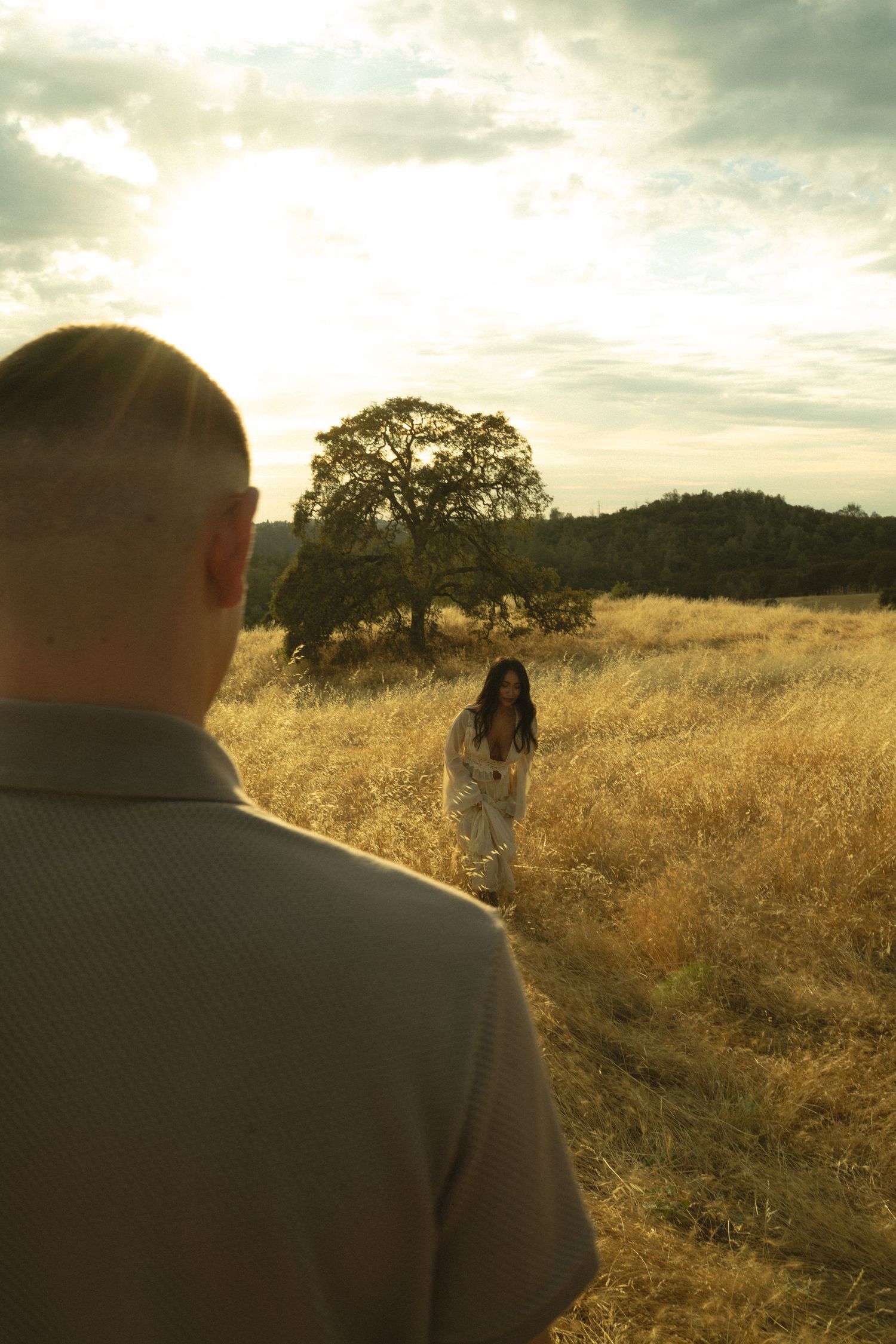 Man watching woman walking toward him through golden sunlit meadow.
