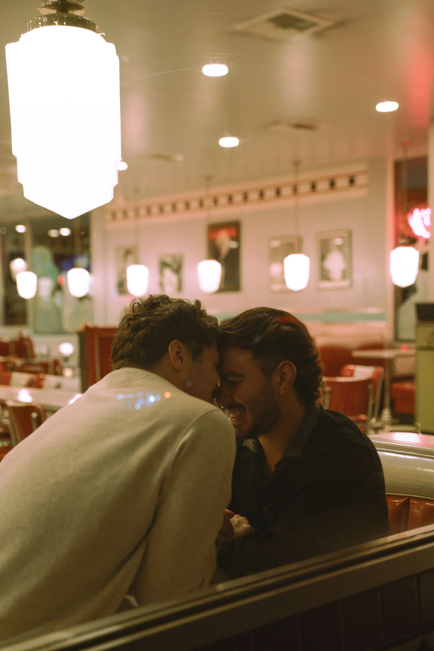 Two people share an intimate moment leaning close together in a warmly lit retro diner booth.