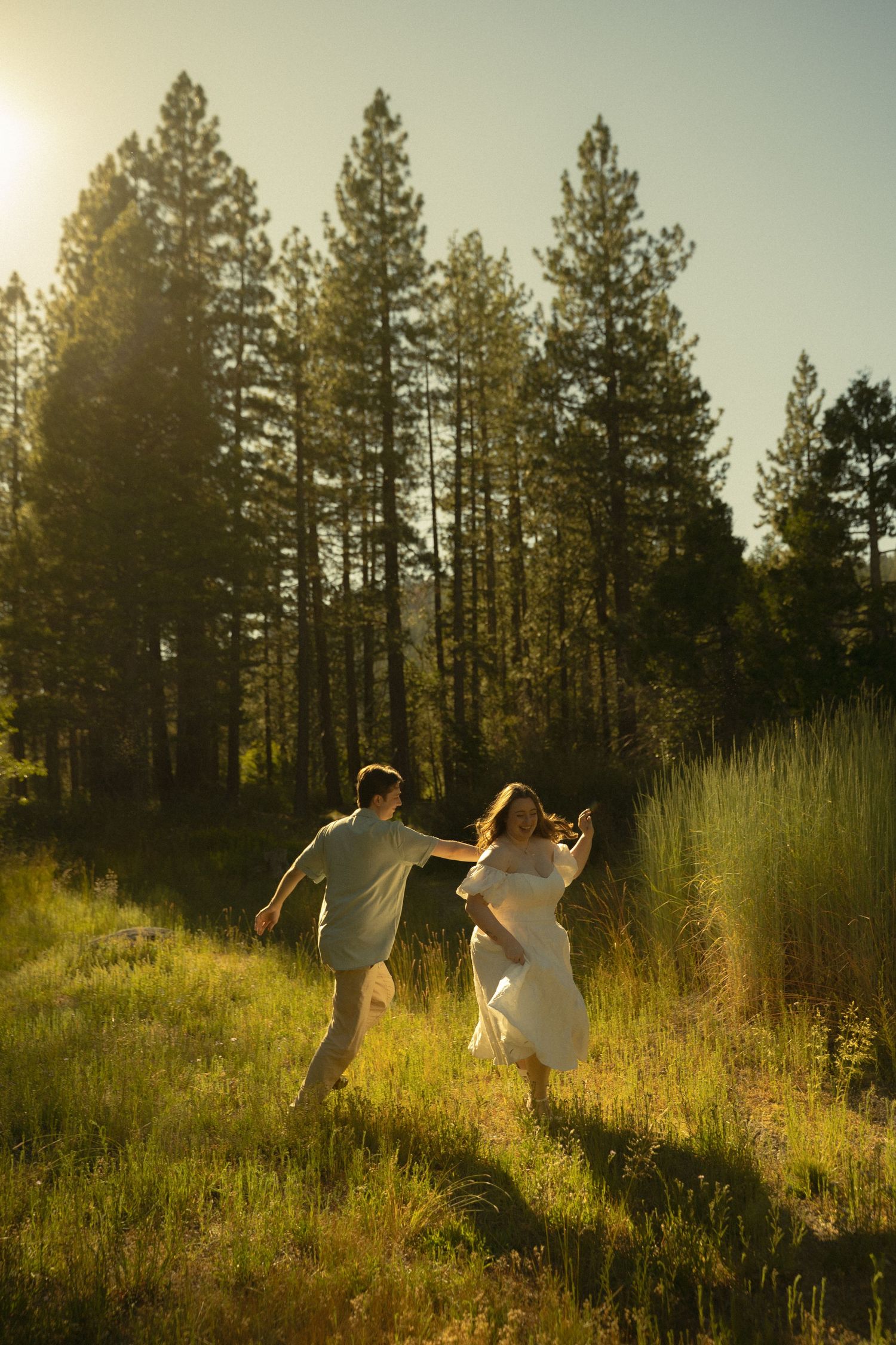 Couple running hand-in-hand through sunlit forest meadow at golden hour.