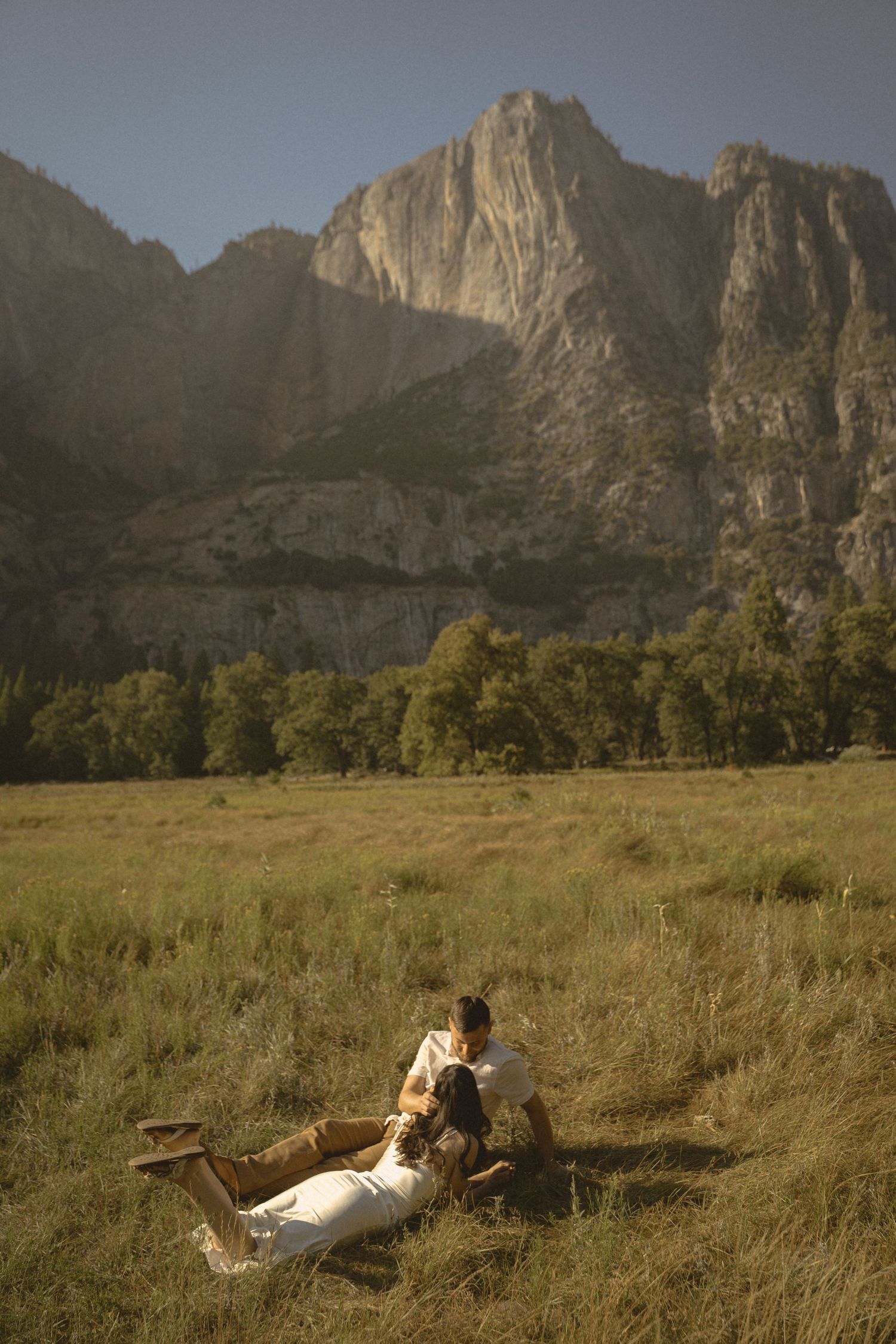 Couple sitting together in a golden meadow with dramatic rocky mountain cliffs in Yosemite Valley.