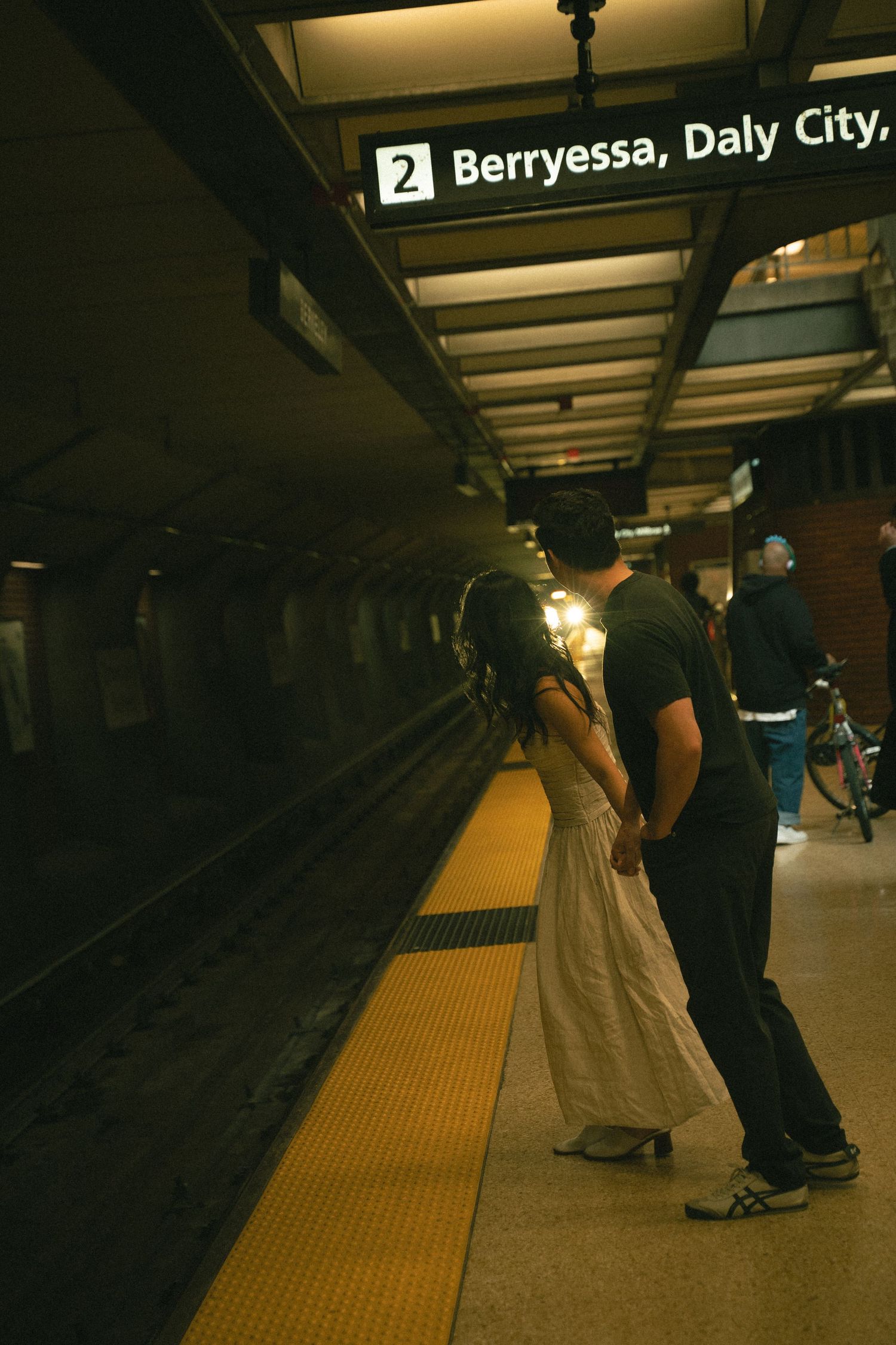 Couple holding hands on a BART platform awaiting a Berryessa Daly City train.