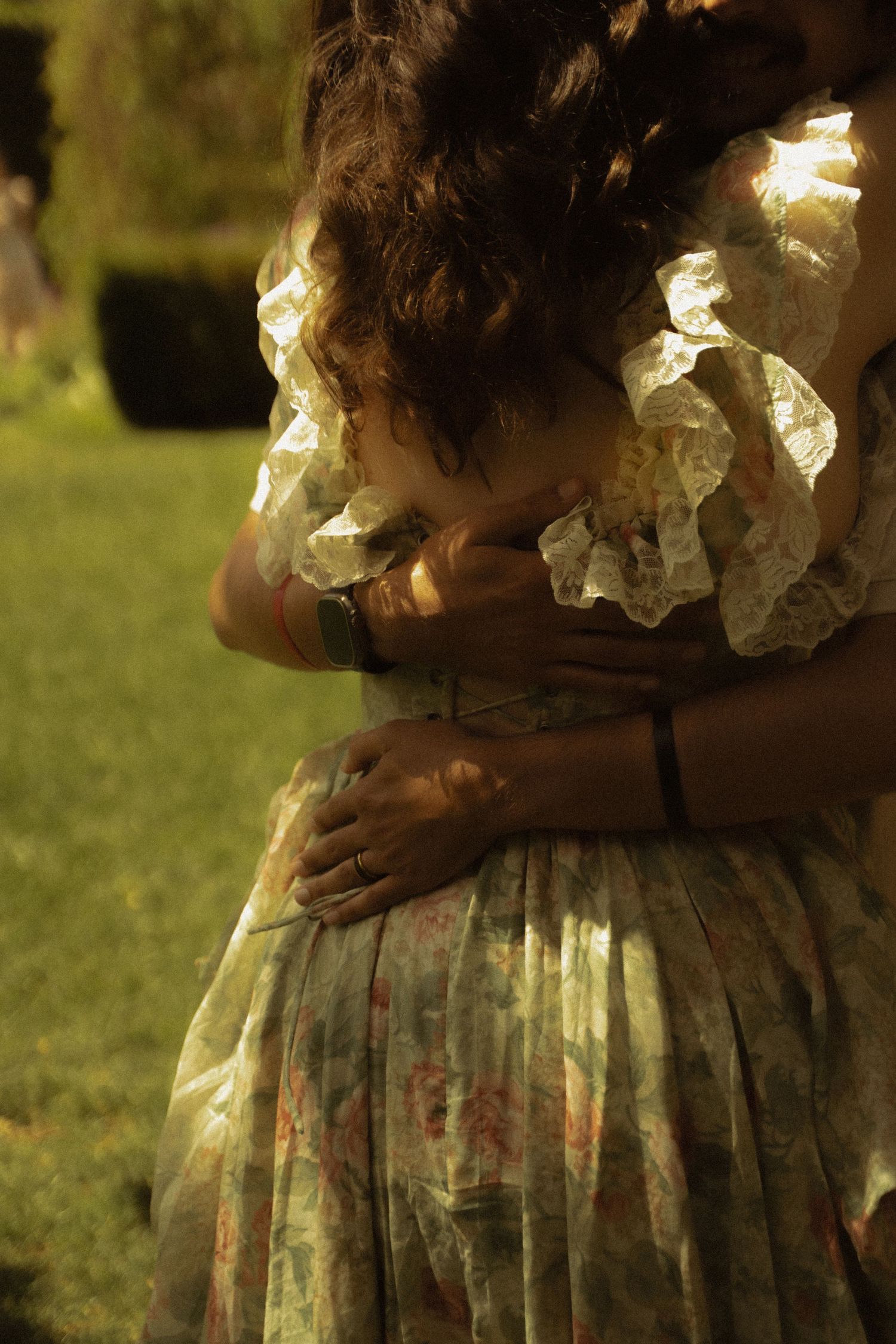 Close-up of couple embracing in sunlit garden, woman wearing vintage lace floral dress.