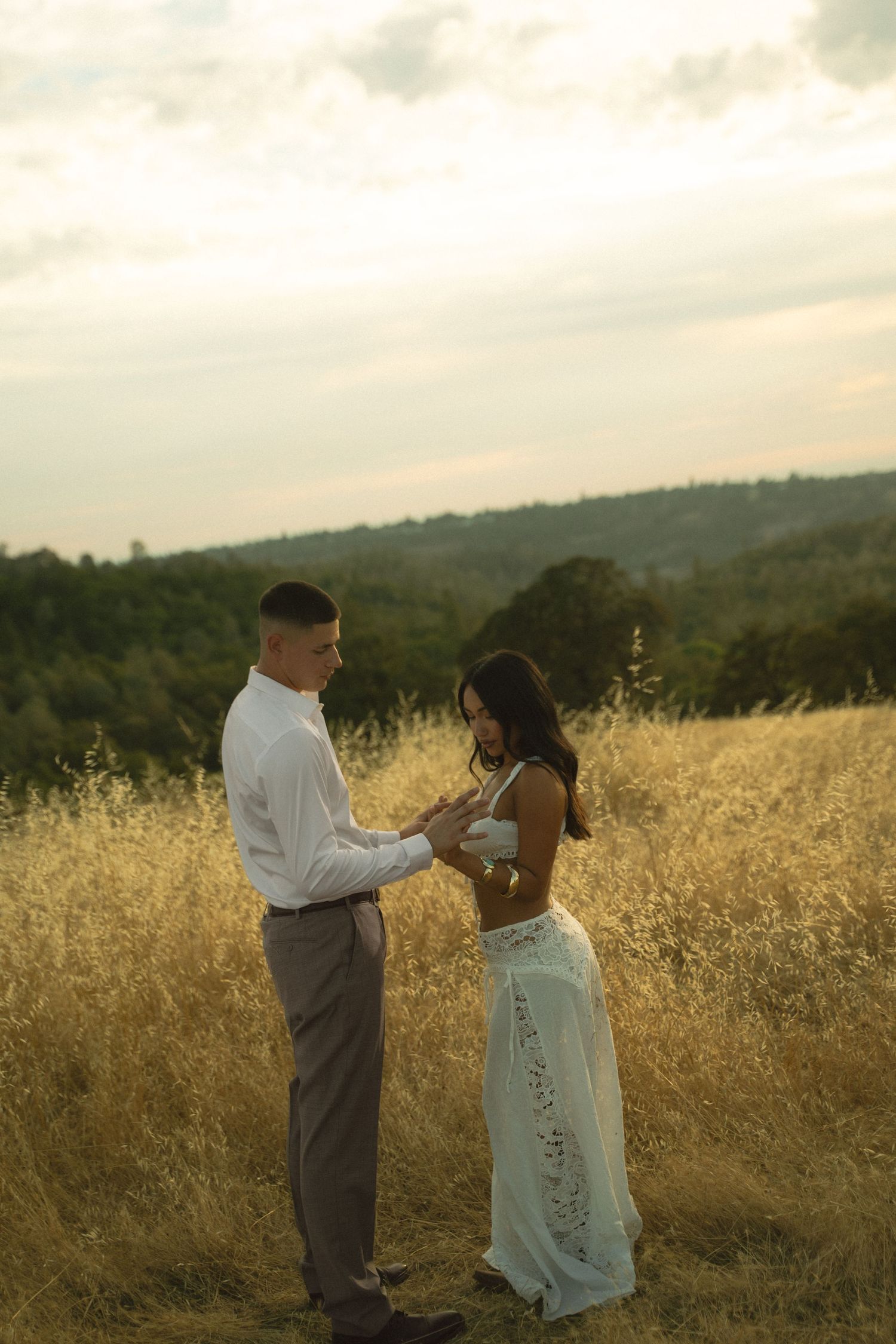 Couple holding hands facing each other in golden field at sunset.