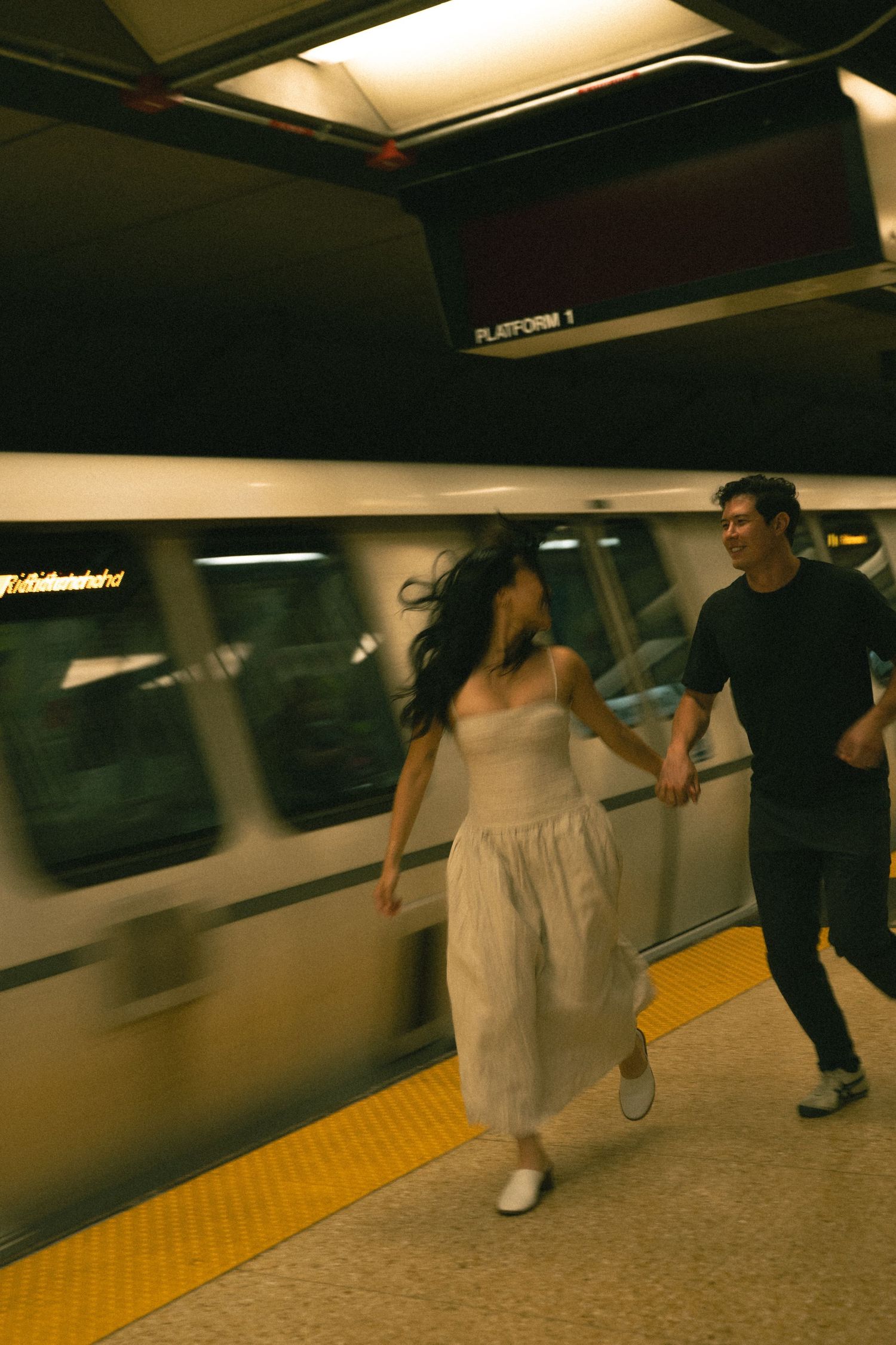 Couple running hand in hand on a subway platform as a train speeds past.