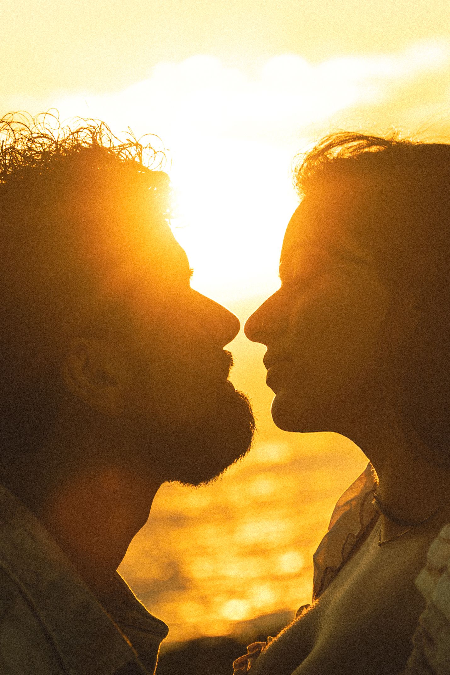 Silhouette of two men about to kiss against a golden sunset backdrop.