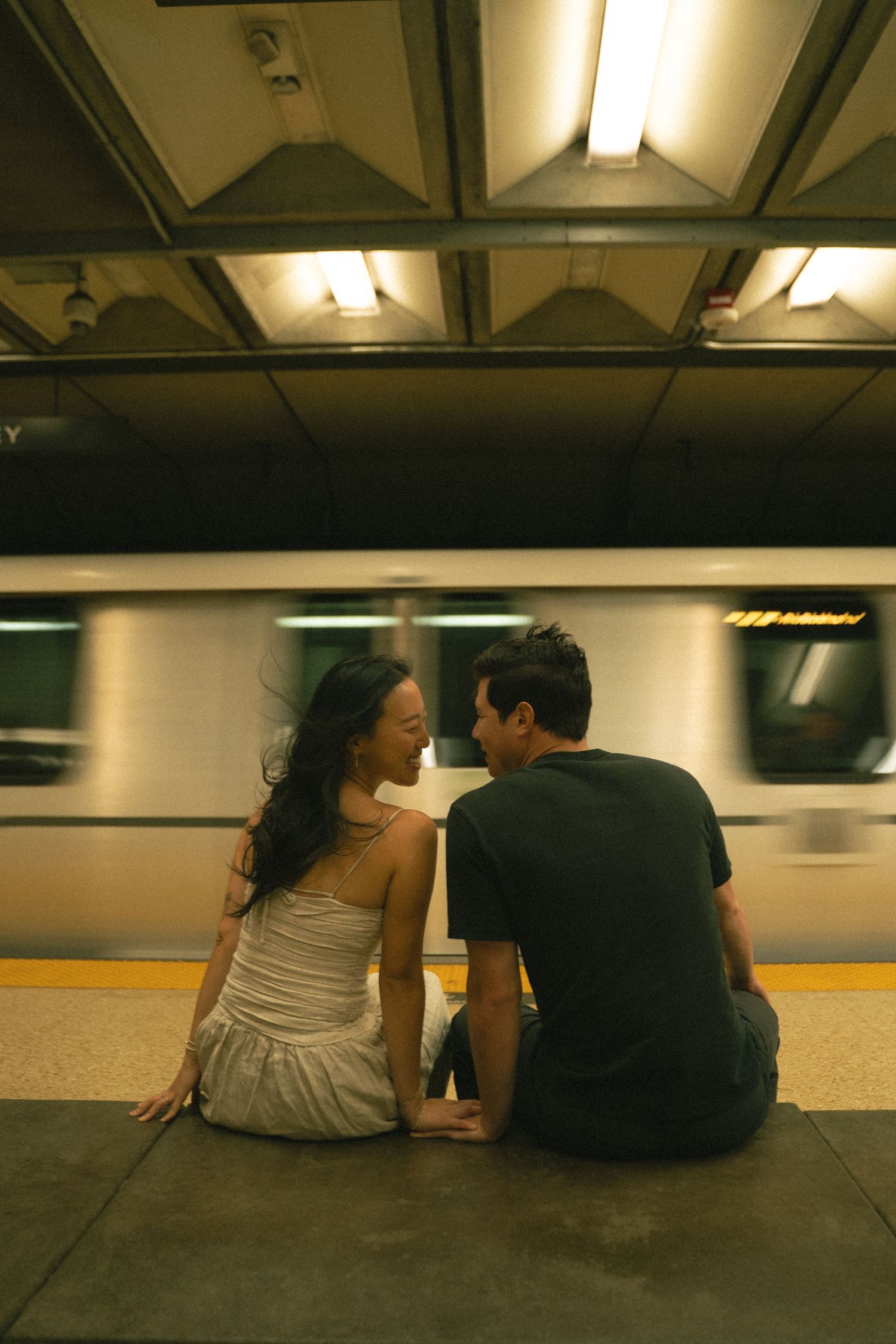 Couple sitting on a subway platform sharing an intimate moment as a train speeds by.