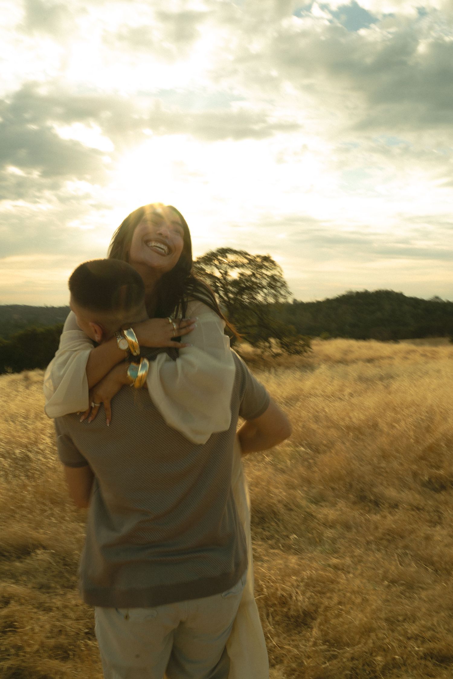Woman laughing joyfully as man lifts her in sun-drenched golden field.