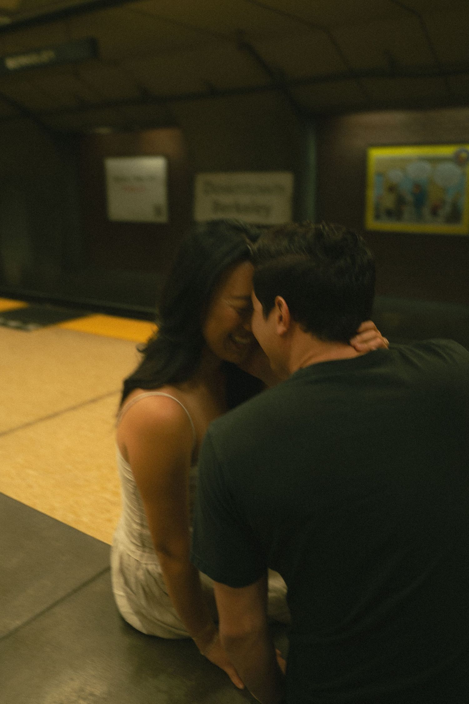 Couple laughing and embracing while sitting on a subway station platform.