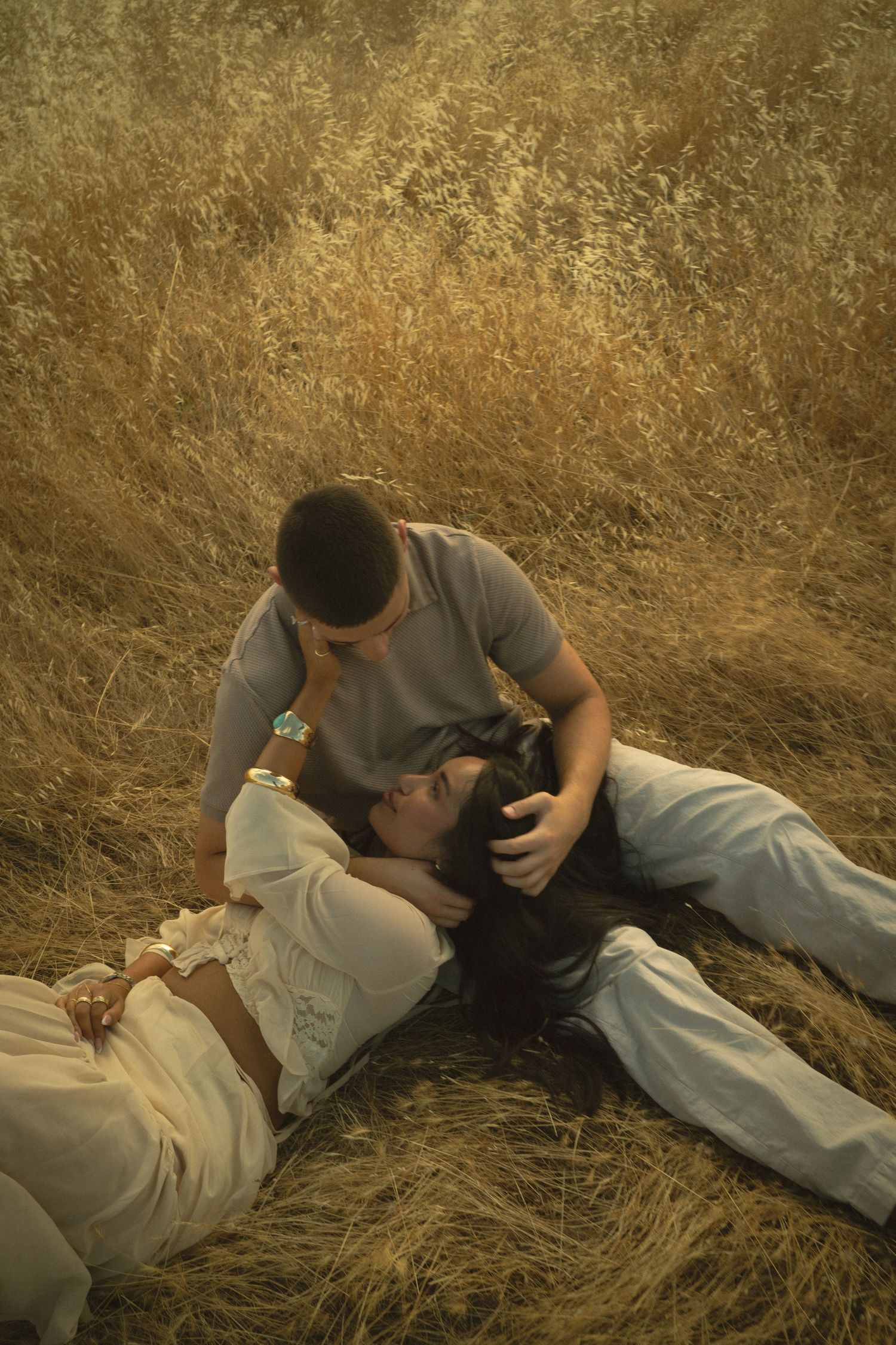 Couple sharing intimate moment in golden wheat field, woman lying down while partner leans over her.