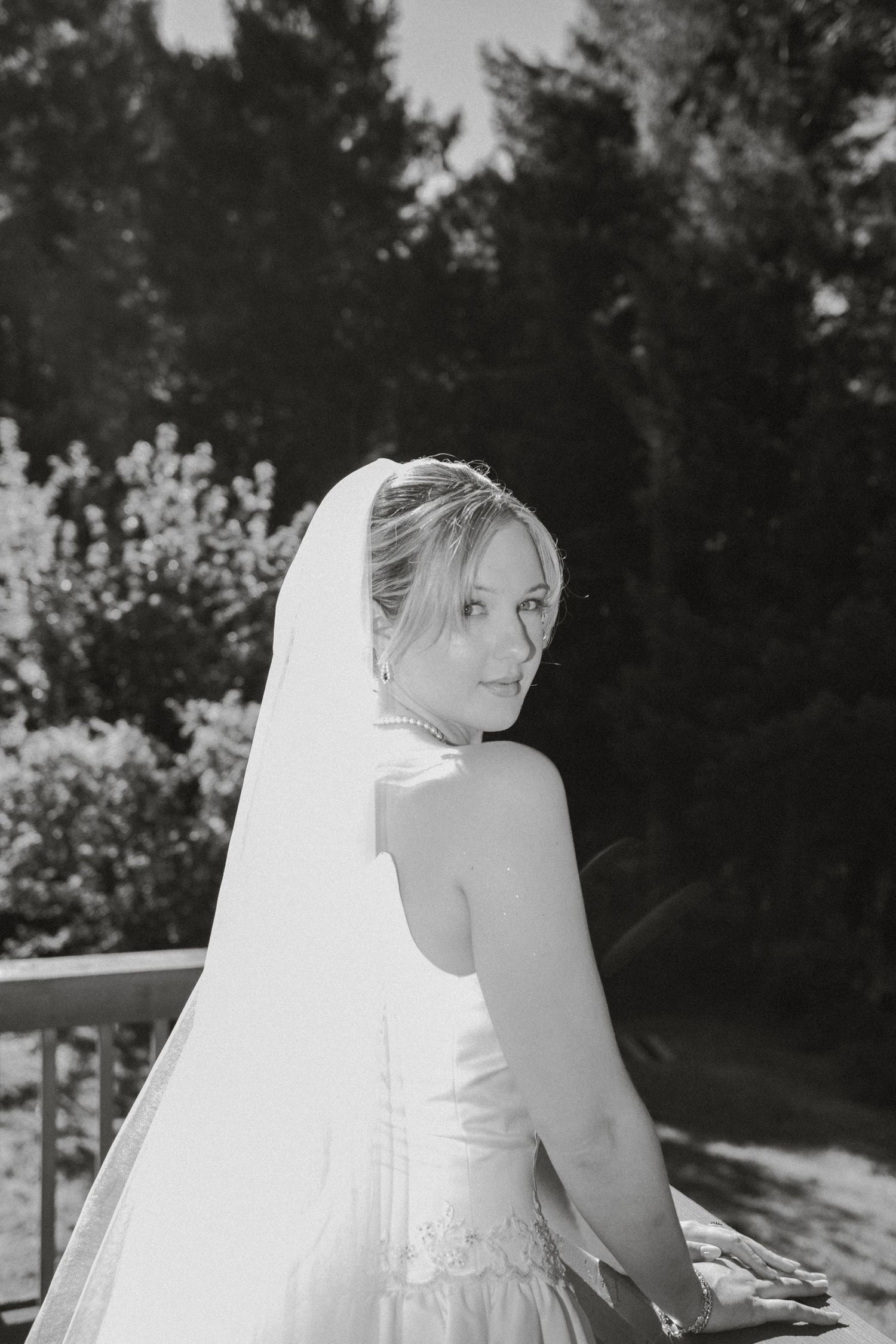 Black and white portrait of a bride in a veil and gown looking back over her shoulder.