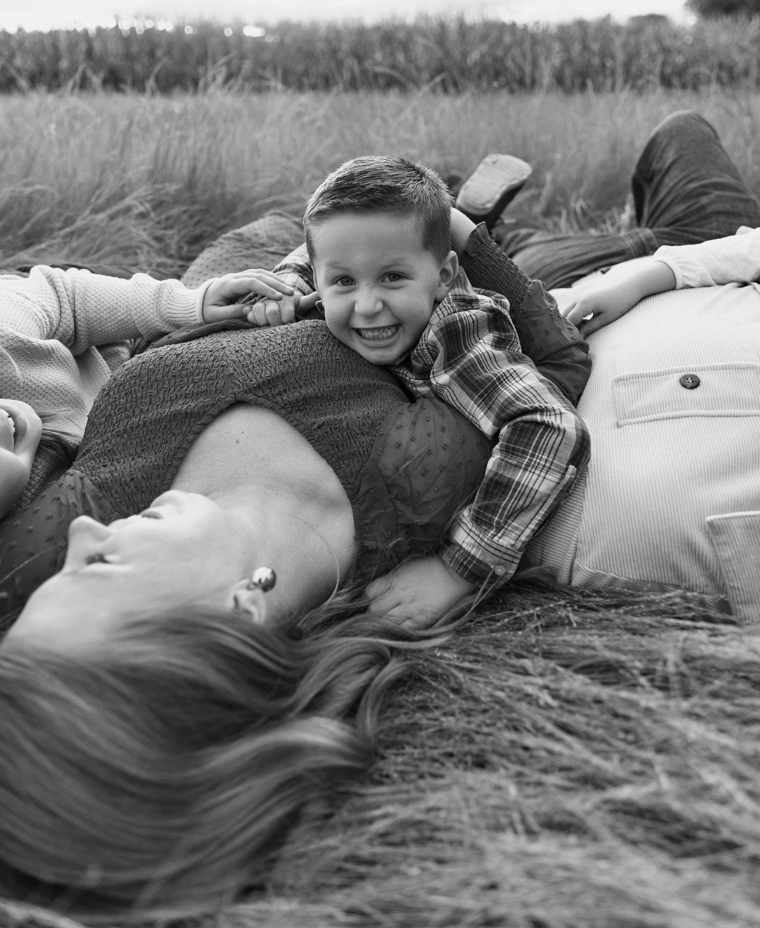 Black and white photo of a laughing boy lying on his mothers chest in a grassy field.