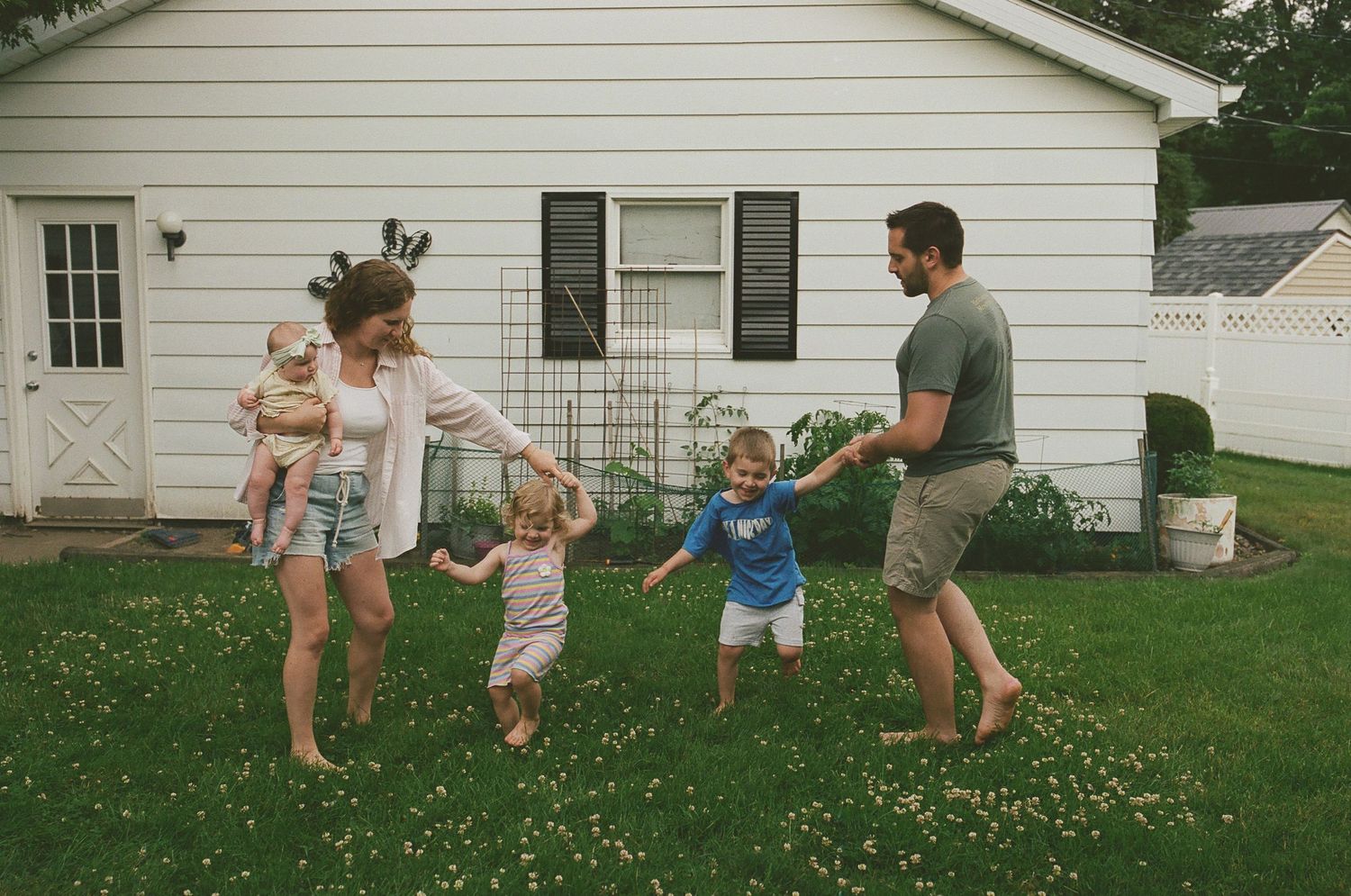 Happy family of five playing together in backyard of white house on summer day.