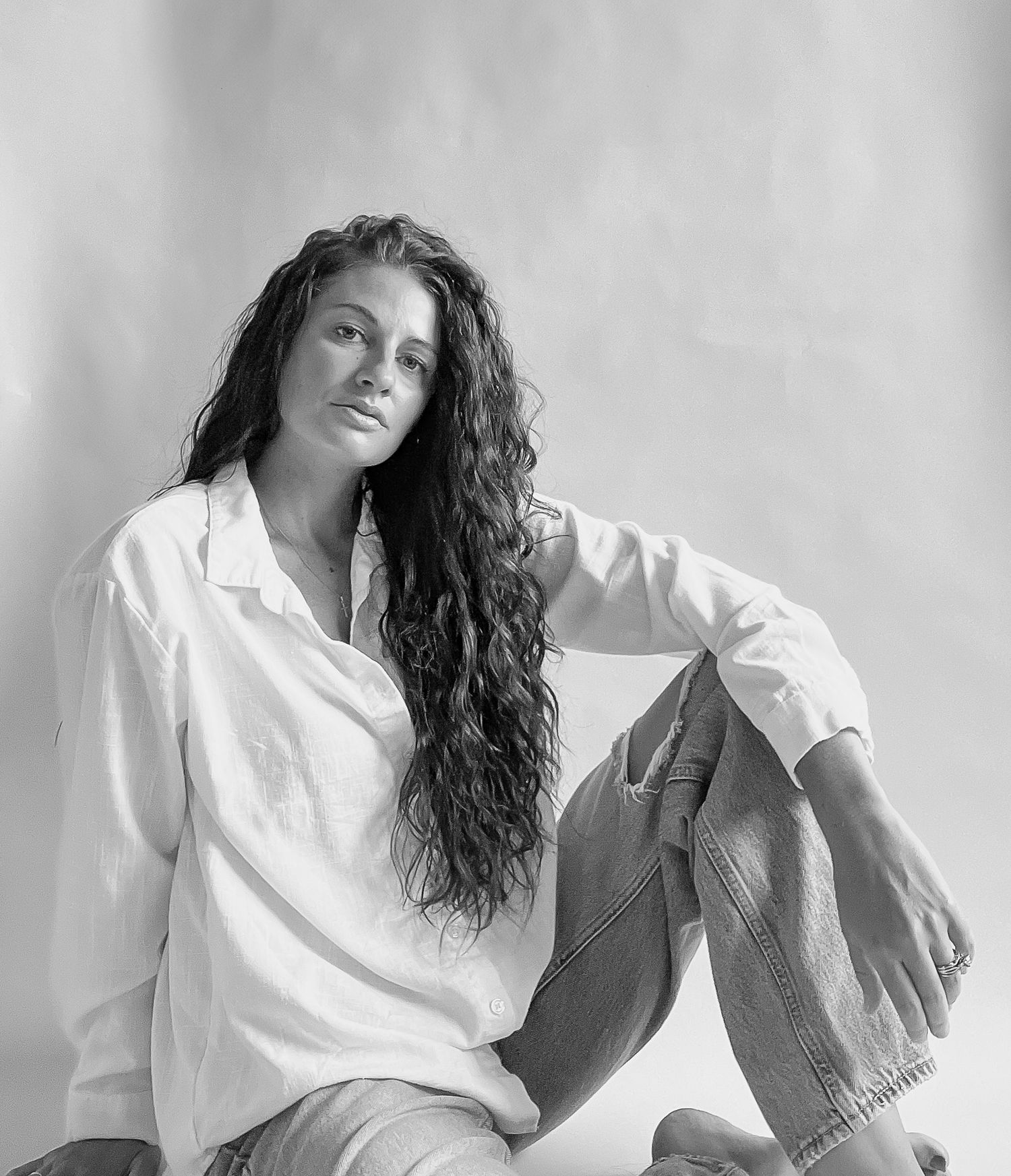 Black and white studio portrait of a young woman with long curly hair wearing a white button-up shirt.