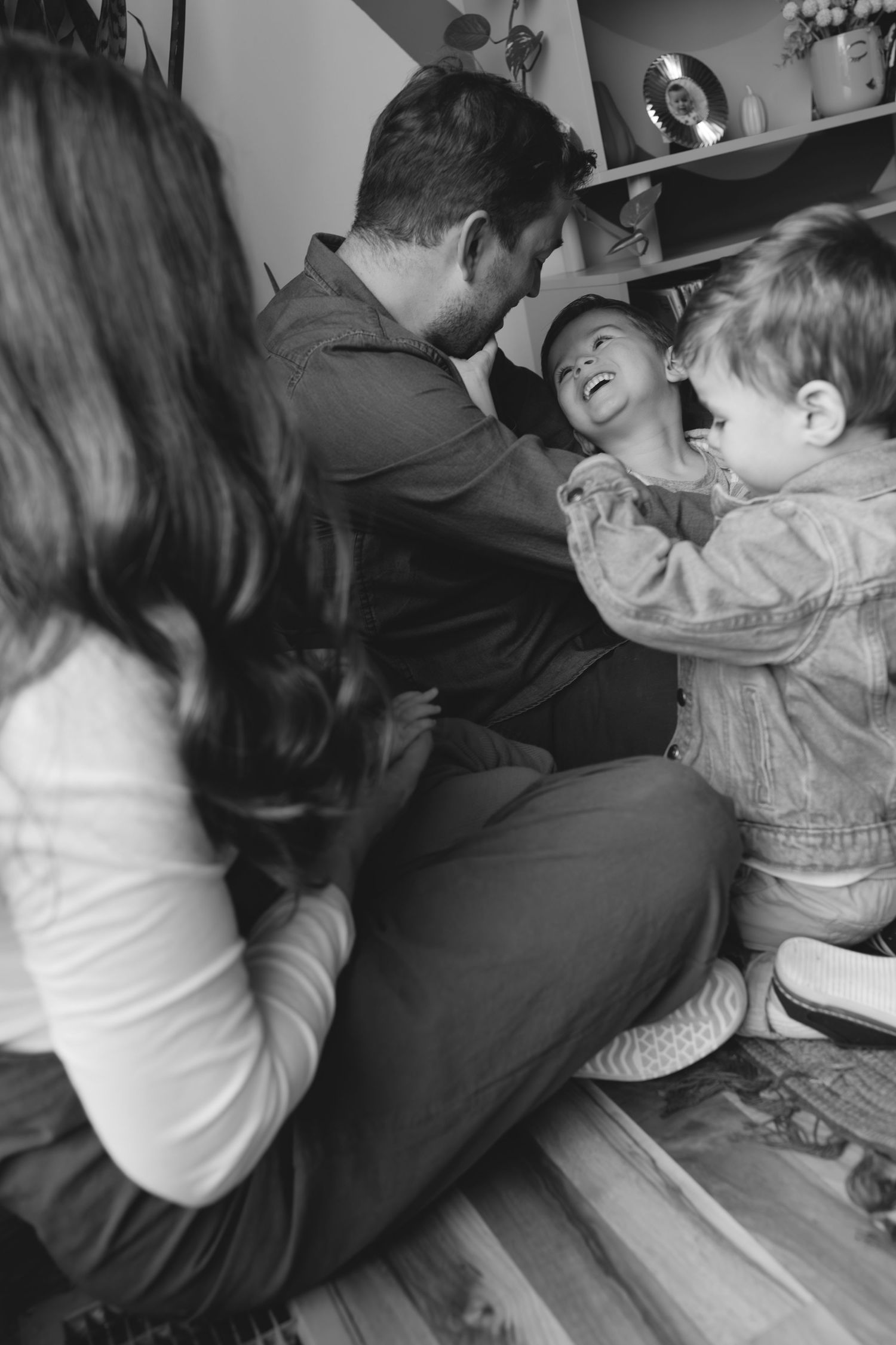 Black and white photo of family playing together on floor indoors with young children.