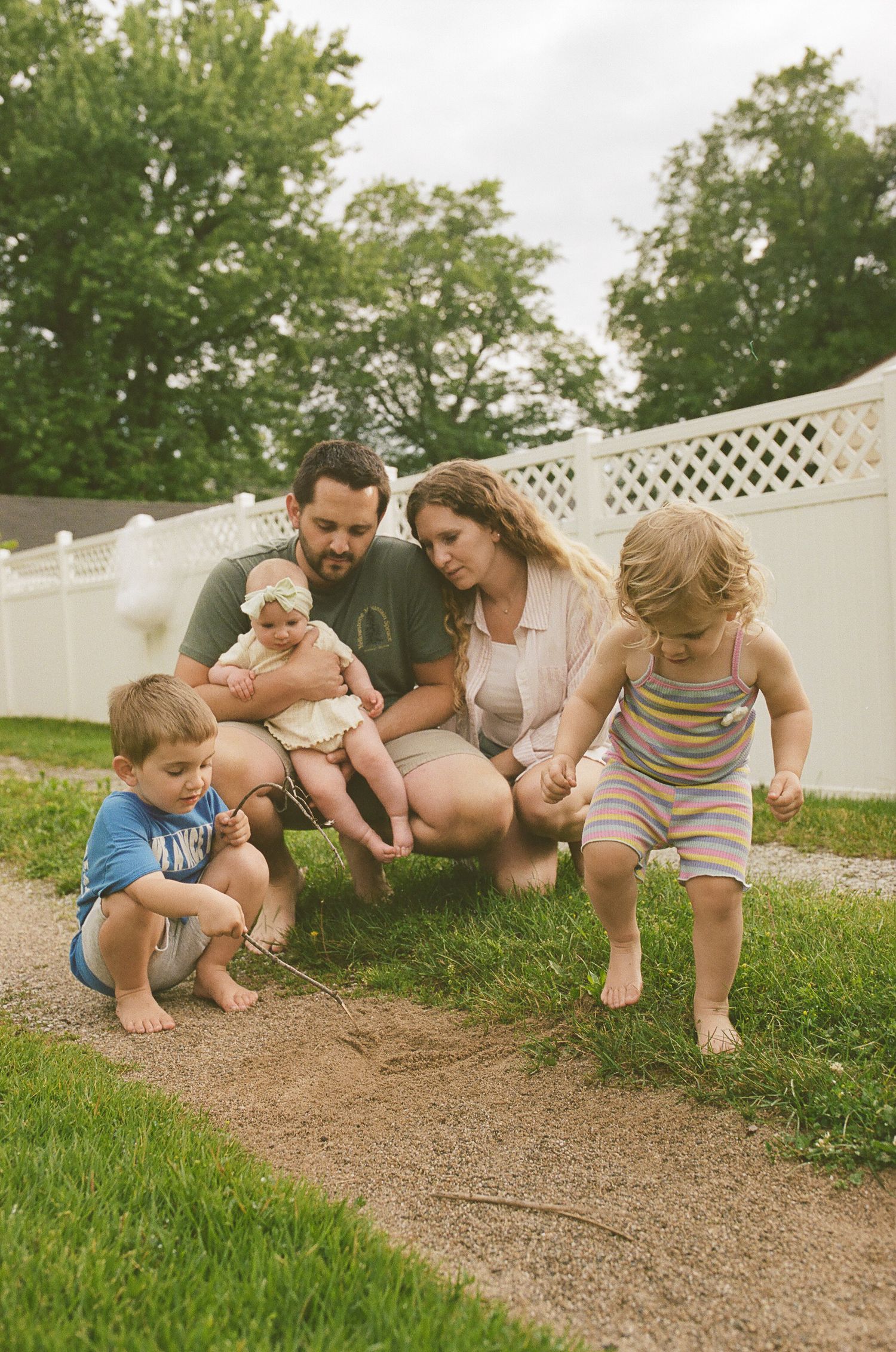 Young family with three children exploring backyard garden path together barefoot.