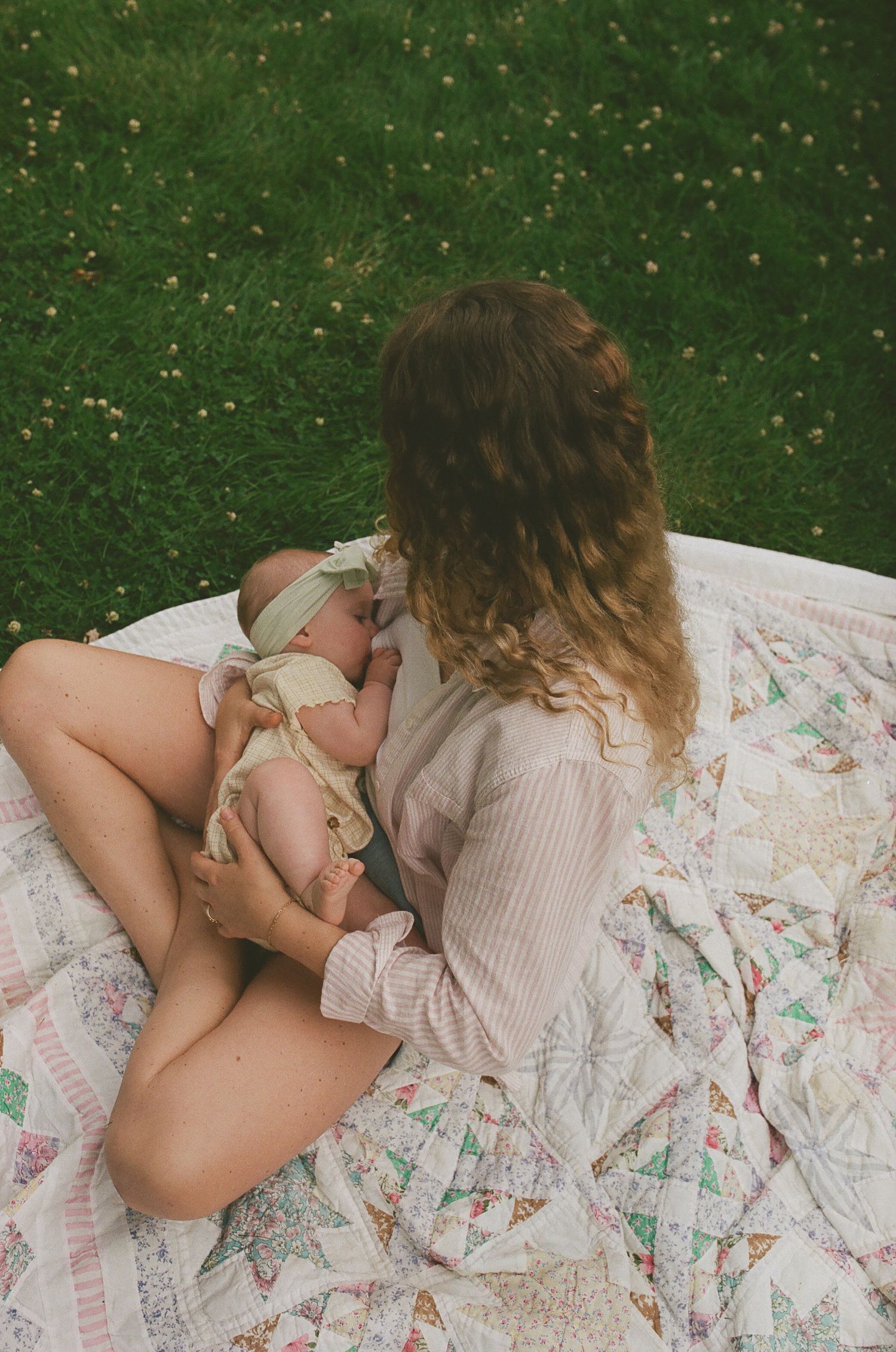Mother breastfeeding newborn baby on vintage patchwork quilt in green garden.