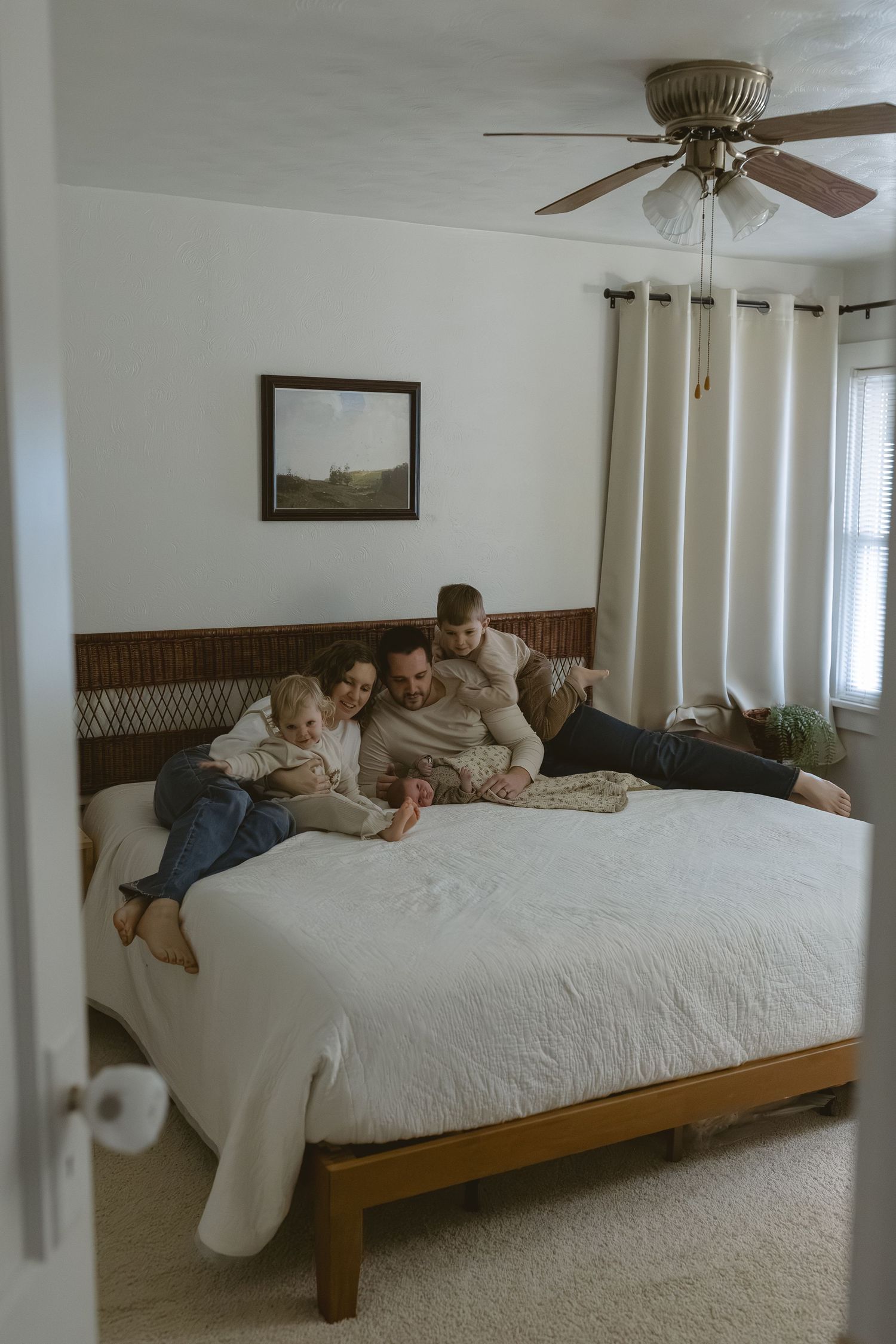 Happy family of four with two young children cuddles together on large bed in cozy bedroom at home.