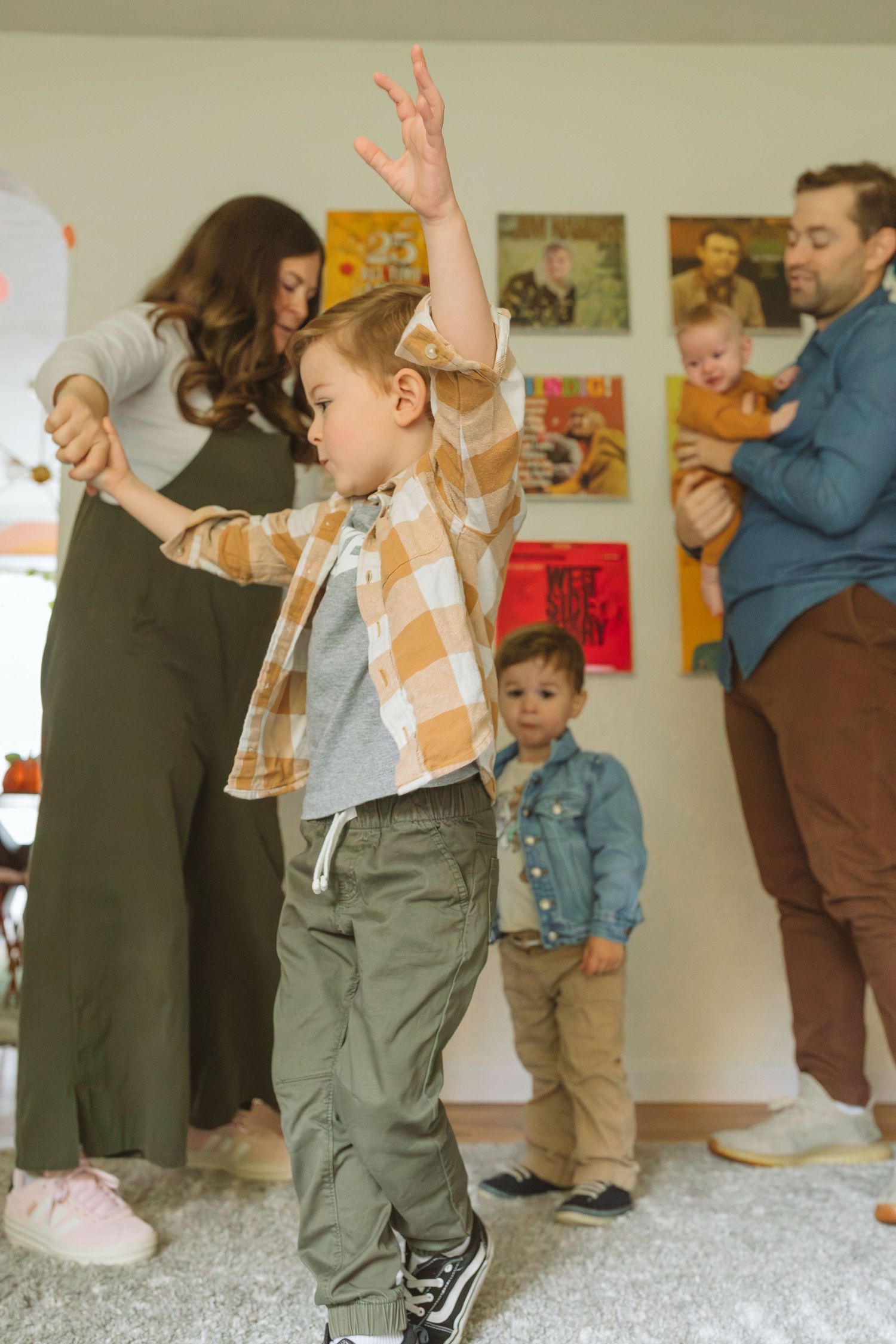 Energetic young boy dancing with raised arms while family plays together in colorful playroom.