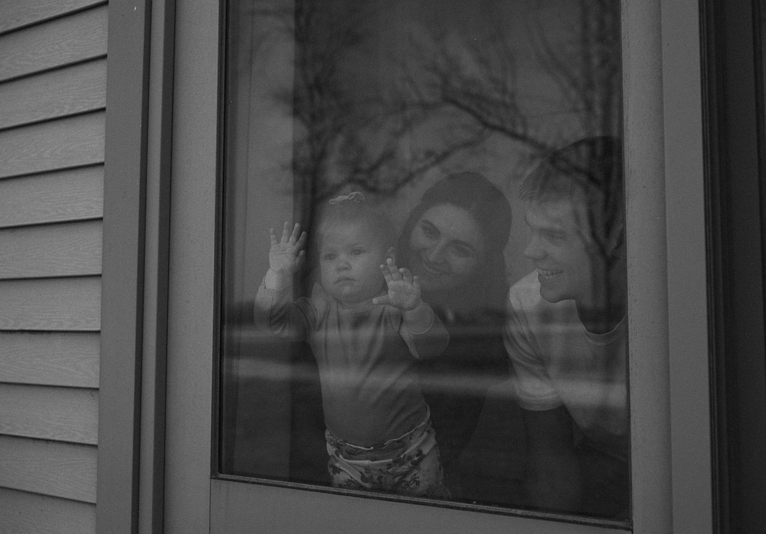 Black and white photo of a mother holding her baby while looking out a home window.