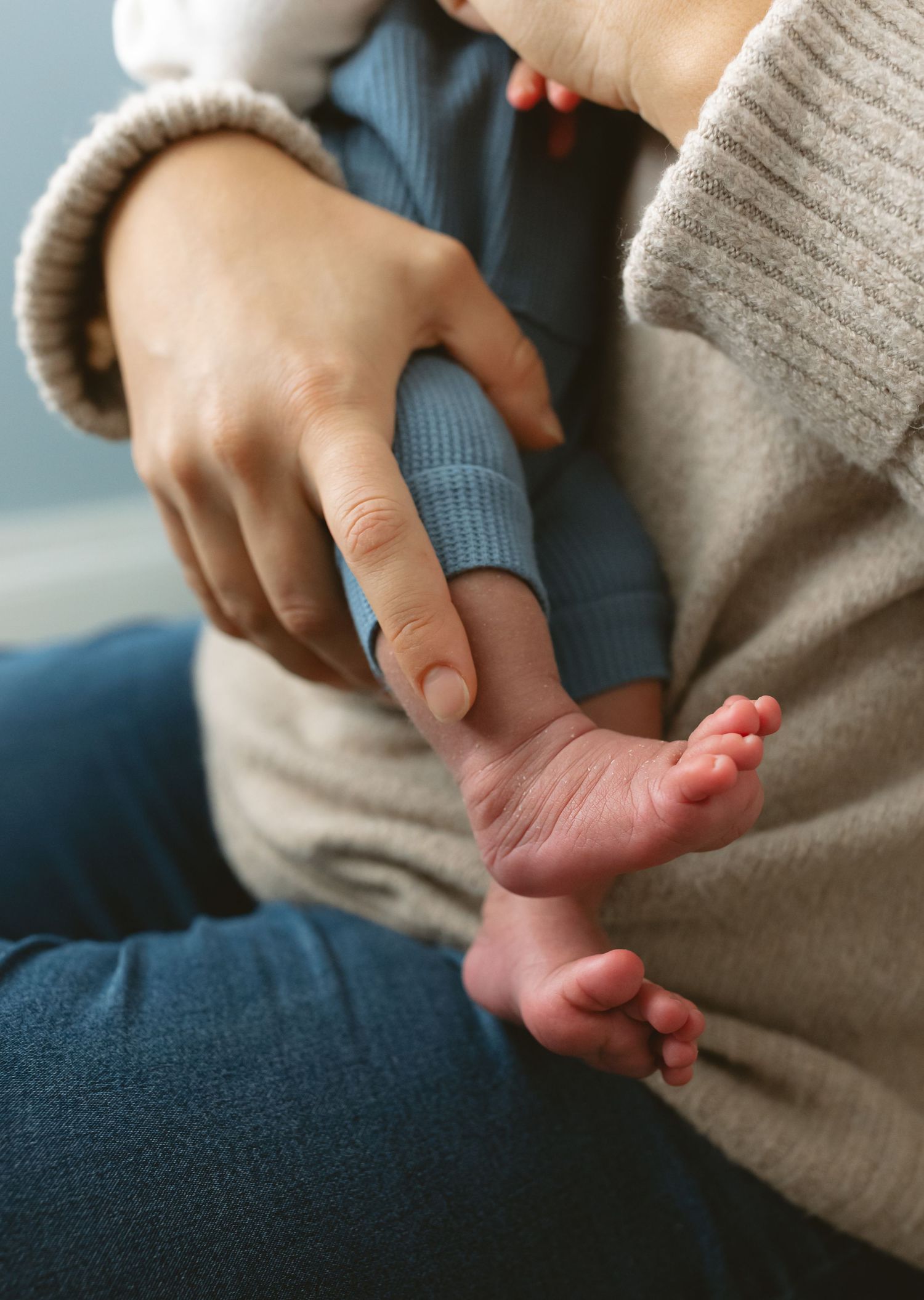 Close-up of parent cradling tiny newborn baby feet in hands while holding infant in cozy knit sweater.