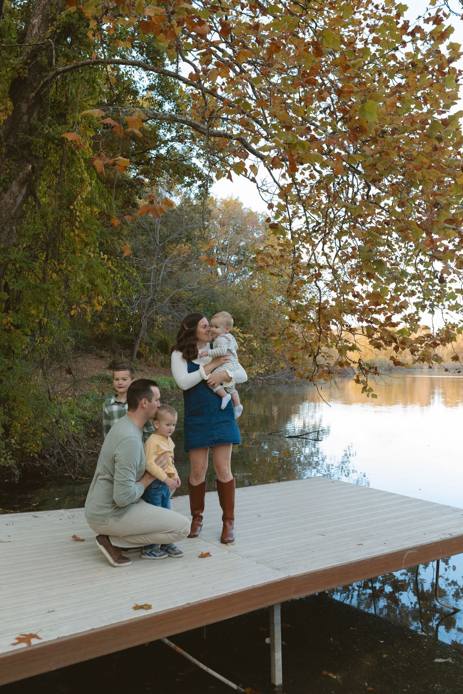 Family of five posing on a wooden dock by a lake surrounded by colorful autumn foliage.
