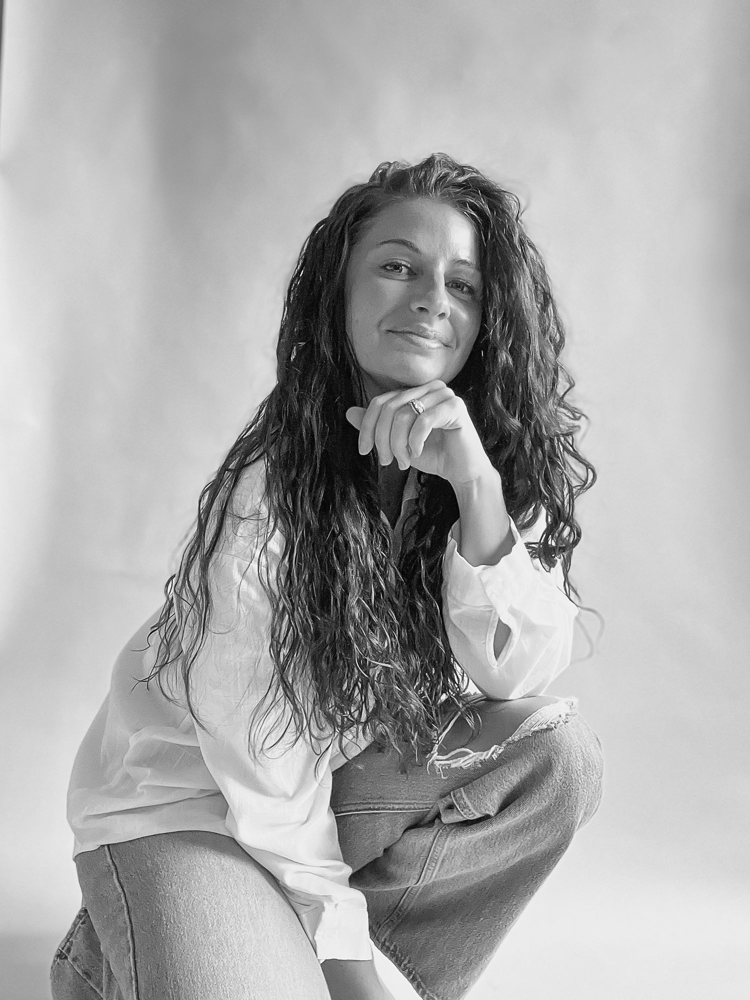 Black and white portrait of a young woman with curly hair posing on white background.