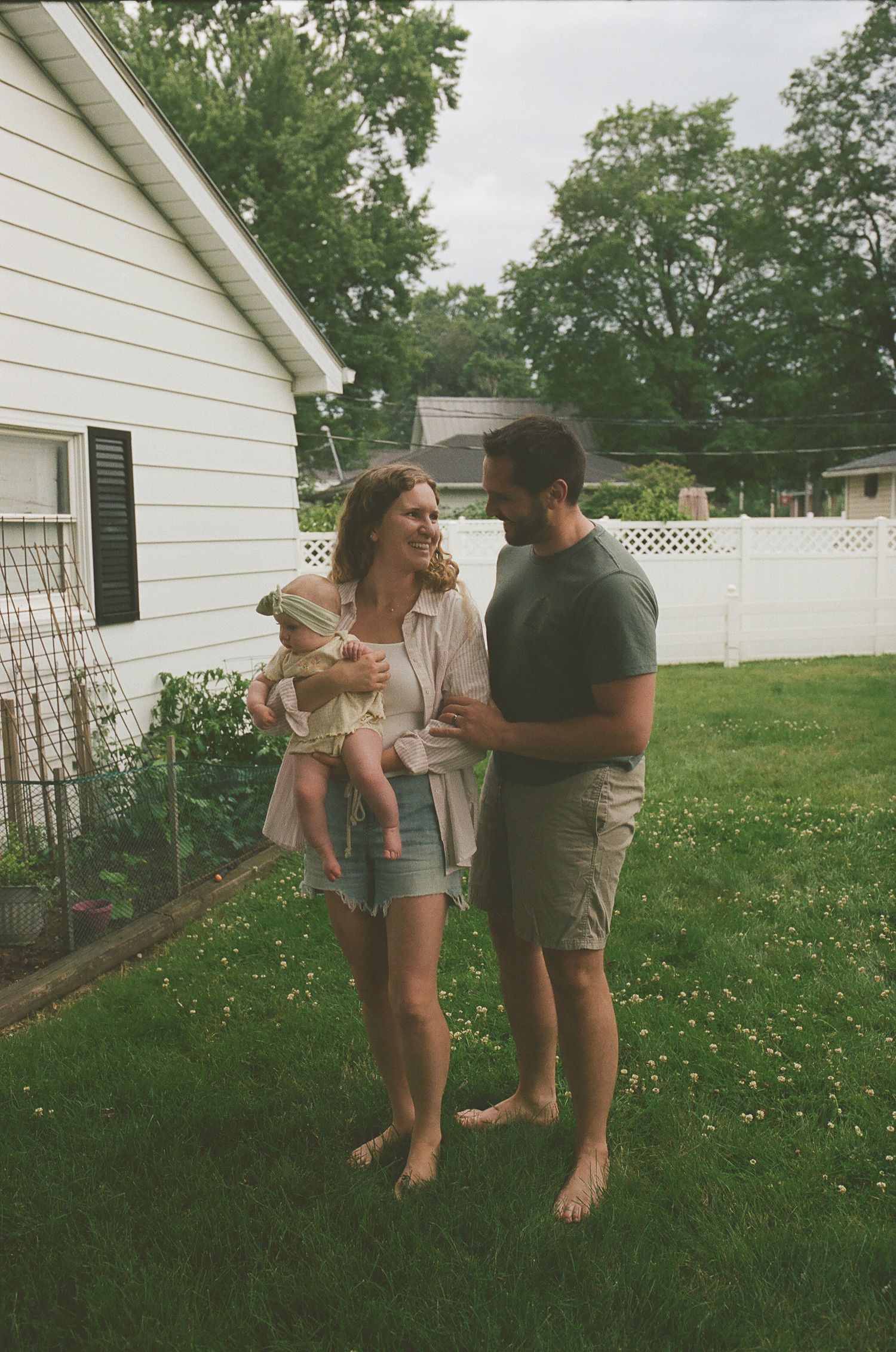 Young couple with newborn baby enjoying sunny day in suburban backyard.