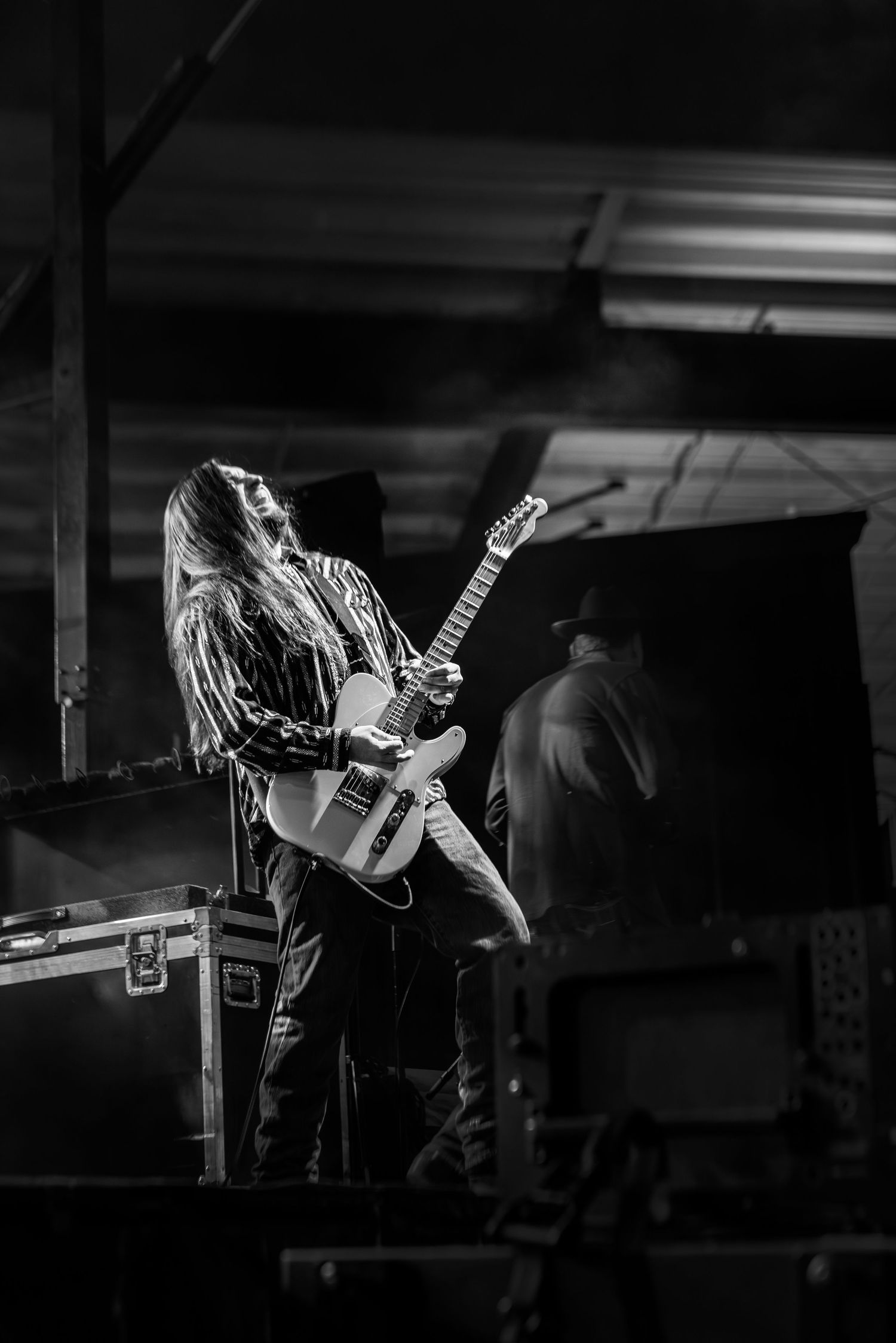 Black and white photo of a long-haired guitarist playing electric guitar on stage at a live music concert.