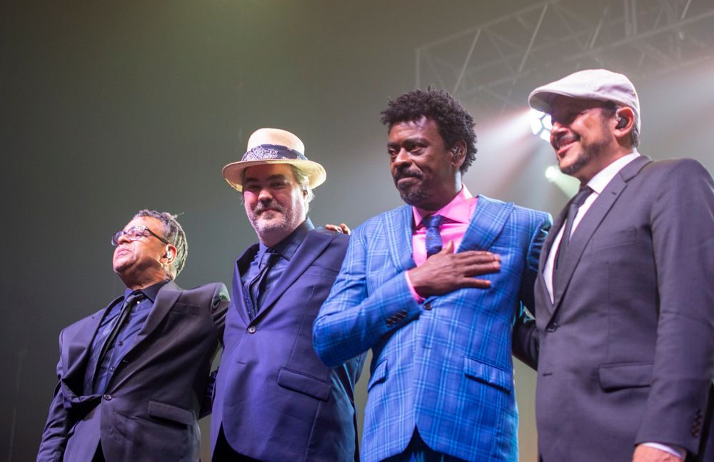 Four male musicians posing together on stage after a live concert performance.