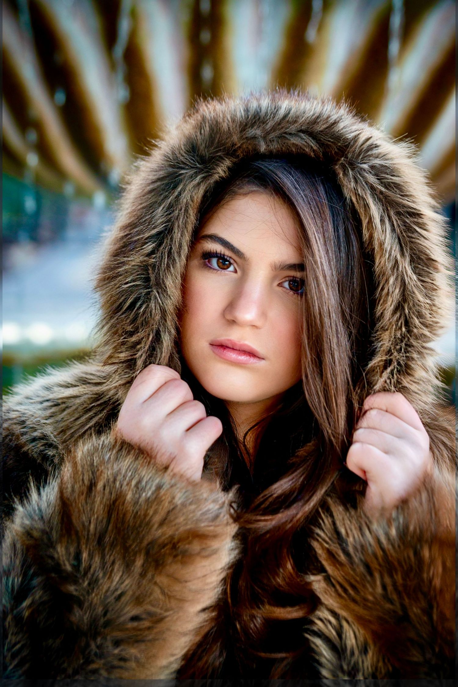 Beautiful young woman wearing brown faux fur hooded coat looking directly at camera.