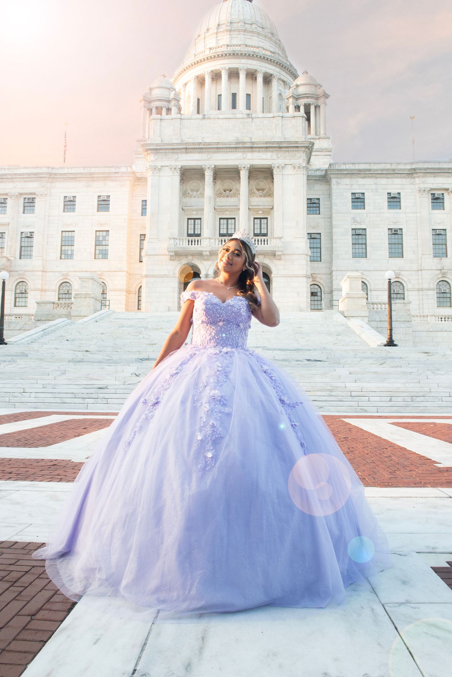 Young woman in lavender quinceañera ball gown posing in front of a grand white capitol building at sunset.