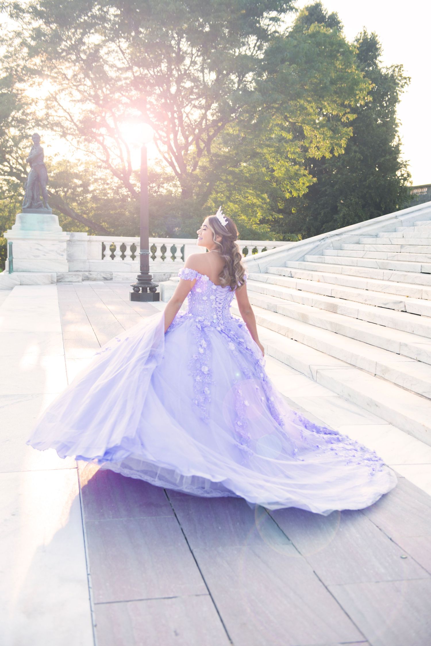 Young woman in a stunning lavender quinceañera gown twirling on marble steps at golden hour sunset.